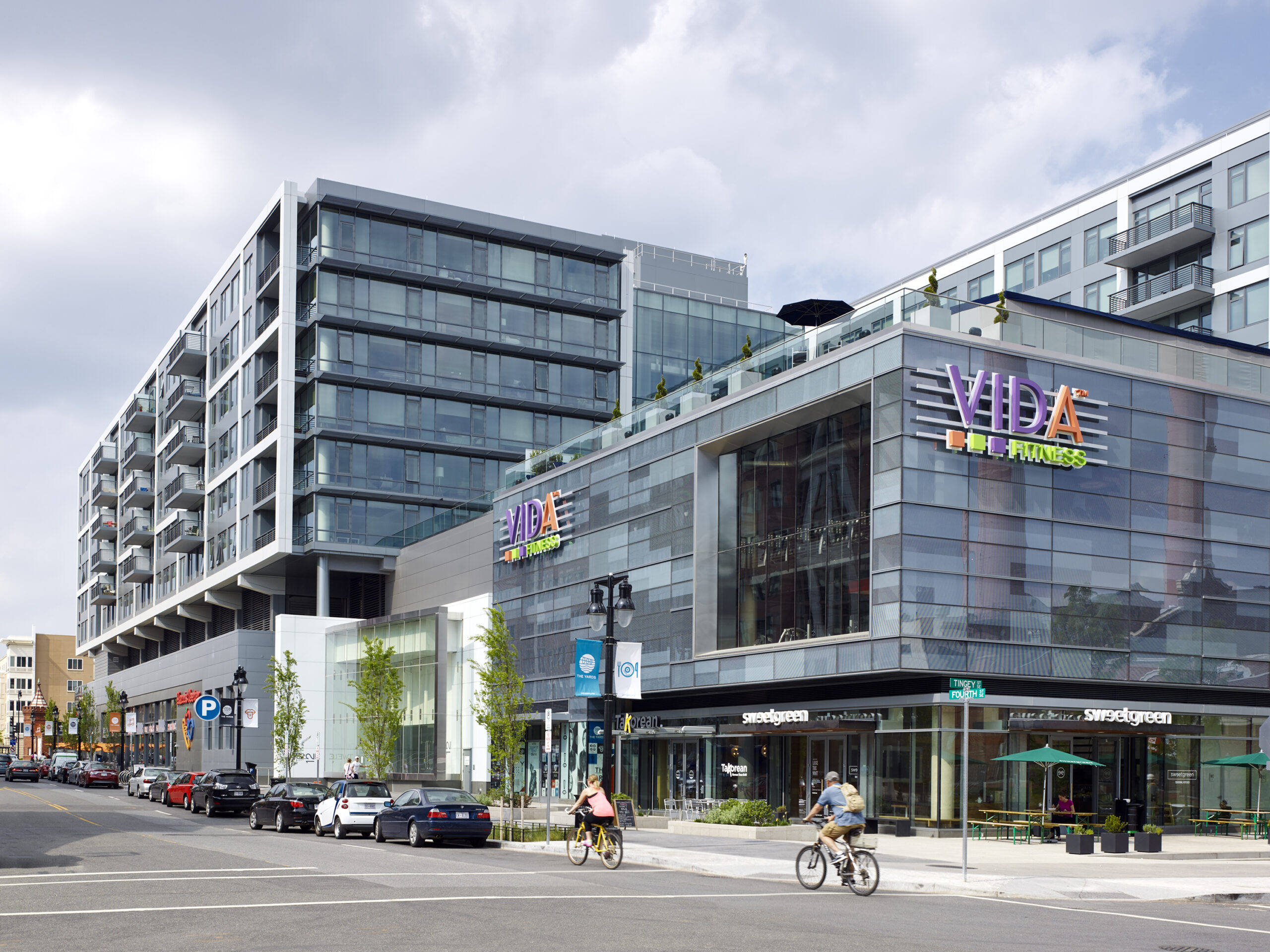 Modern mixed-use building with residential units, shops, and VIDA Fitness on a busy city street.