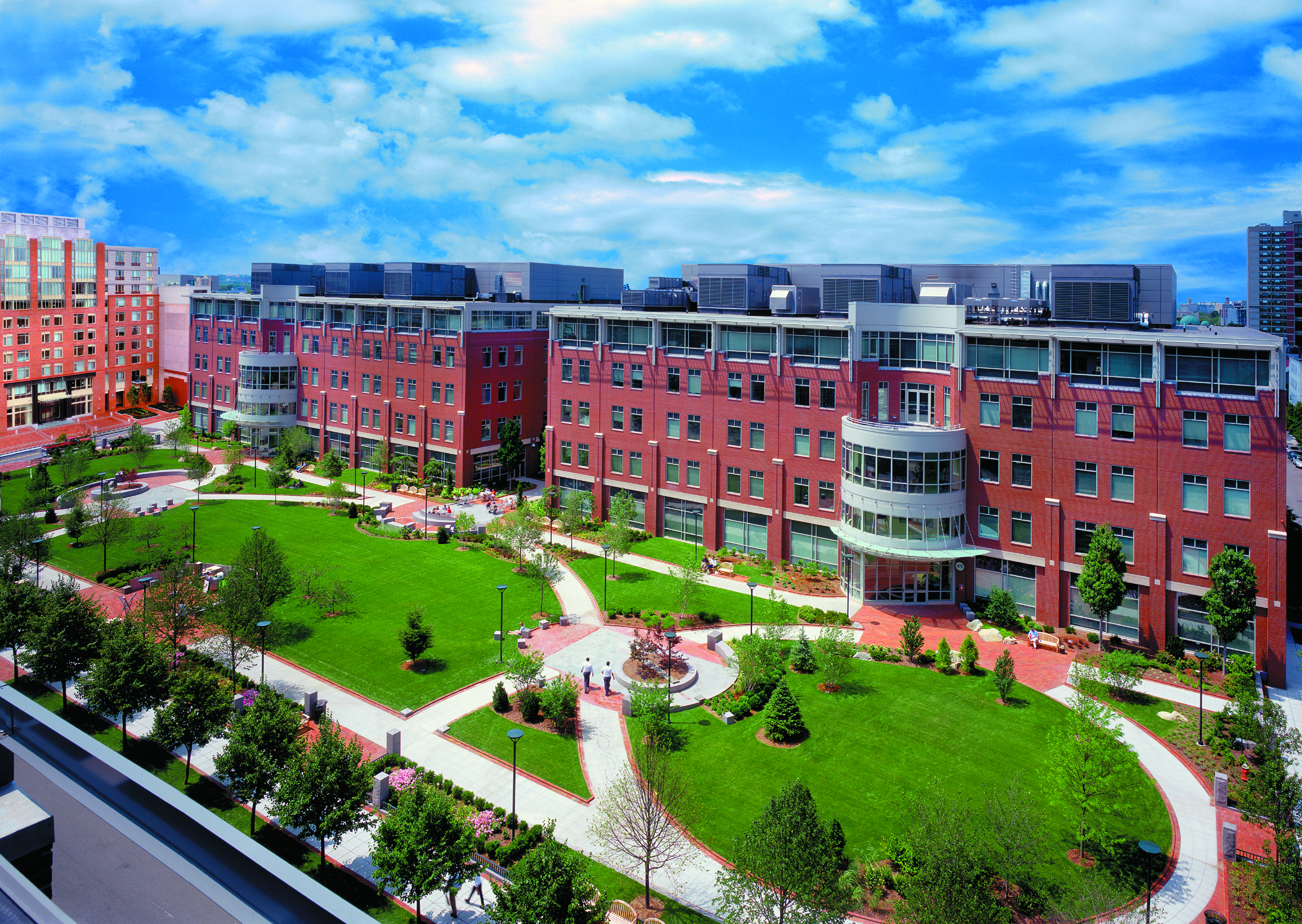 Landscaped green space with red brick office buildings on the right and 91 Sidney apartments to the far left.