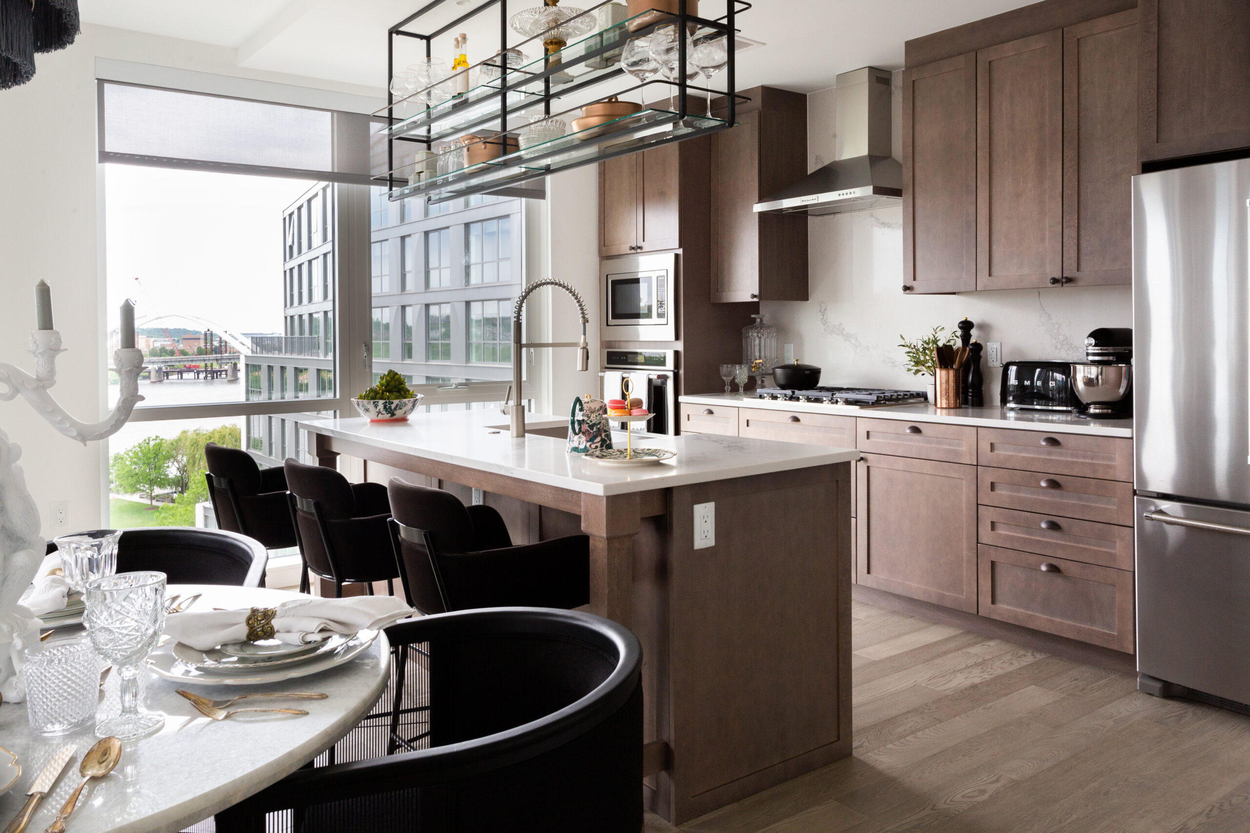 Modern kitchen with stainless steel appliances, a large island, and an elegant dining table. Floor-to-ceiling windows offer a view of the city.