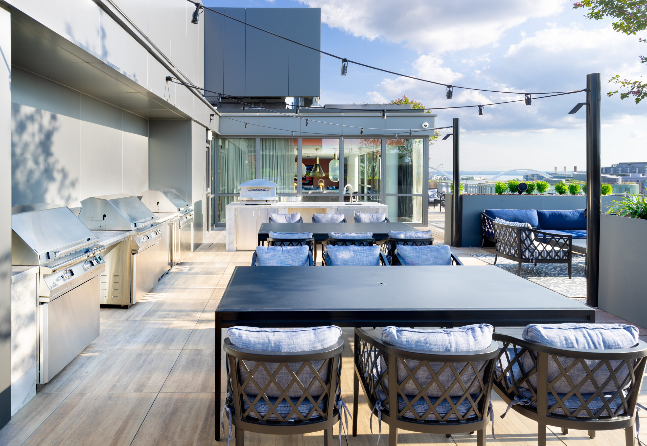 Outdoor rooftop lounge with BBQ grills, dining tables, and comfortable seating, offering views of the surrounding area.