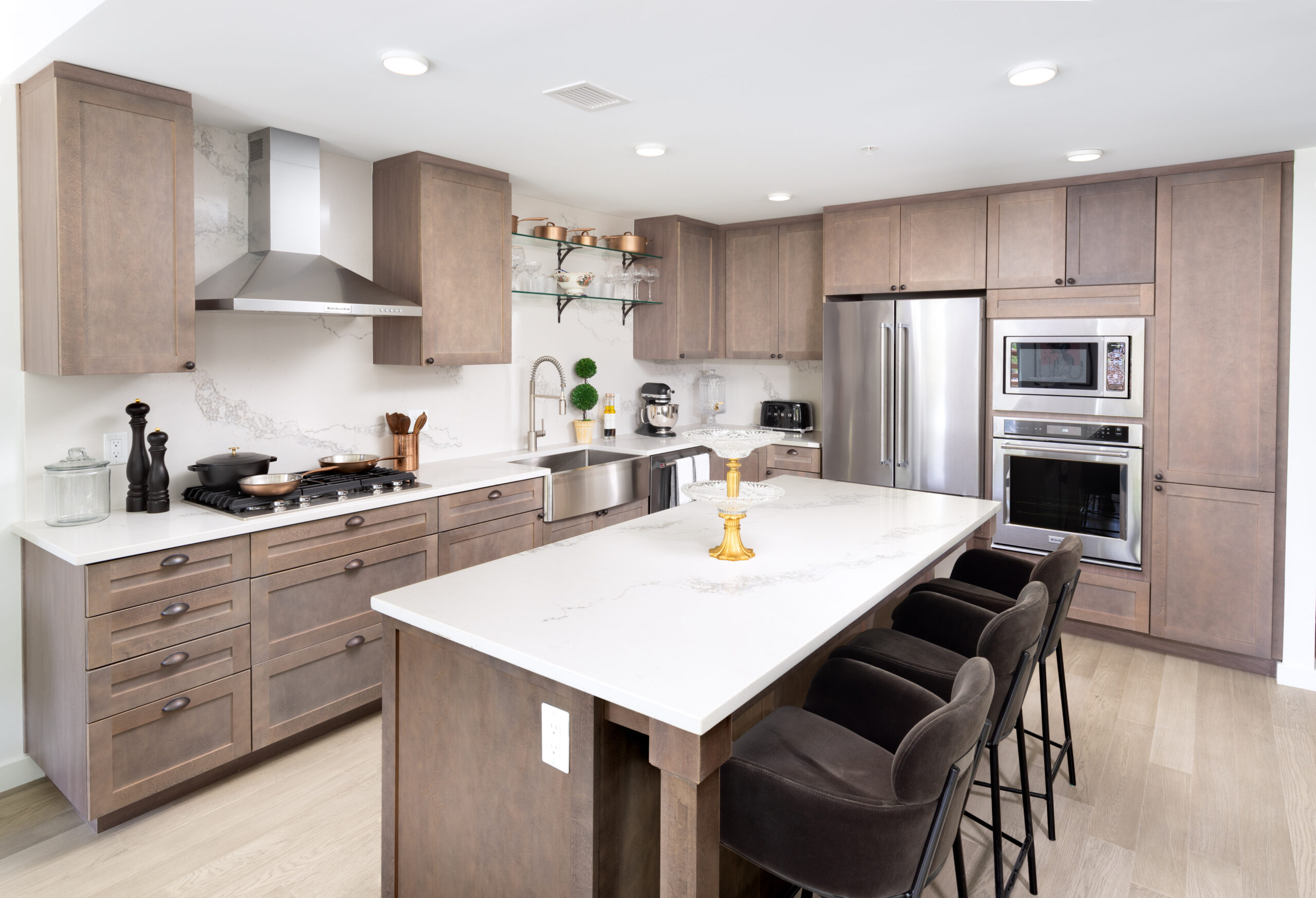 Modern kitchen with stainless steel appliances, a large marble island, and sleek wooden cabinets. Black velvet bar stools line the island for seating.