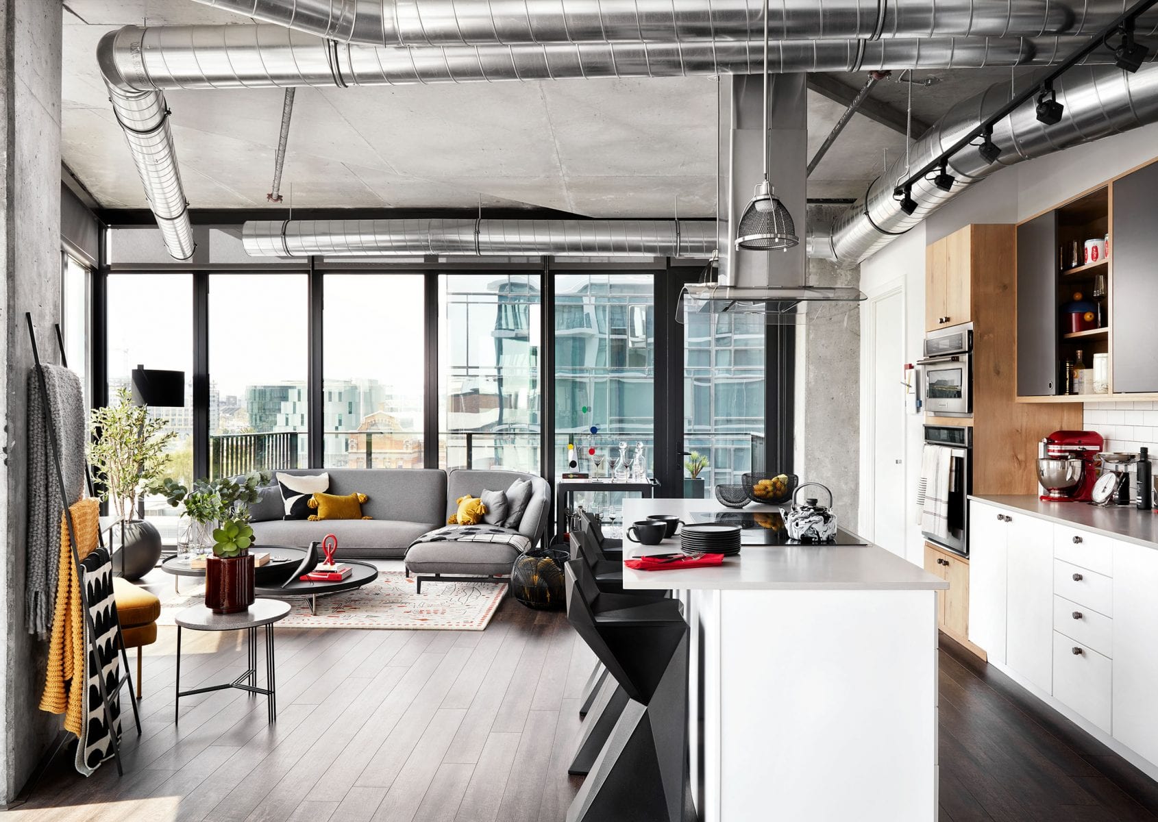 Open-concept living area with large windows, industrial ductwork, and a sleek kitchen.