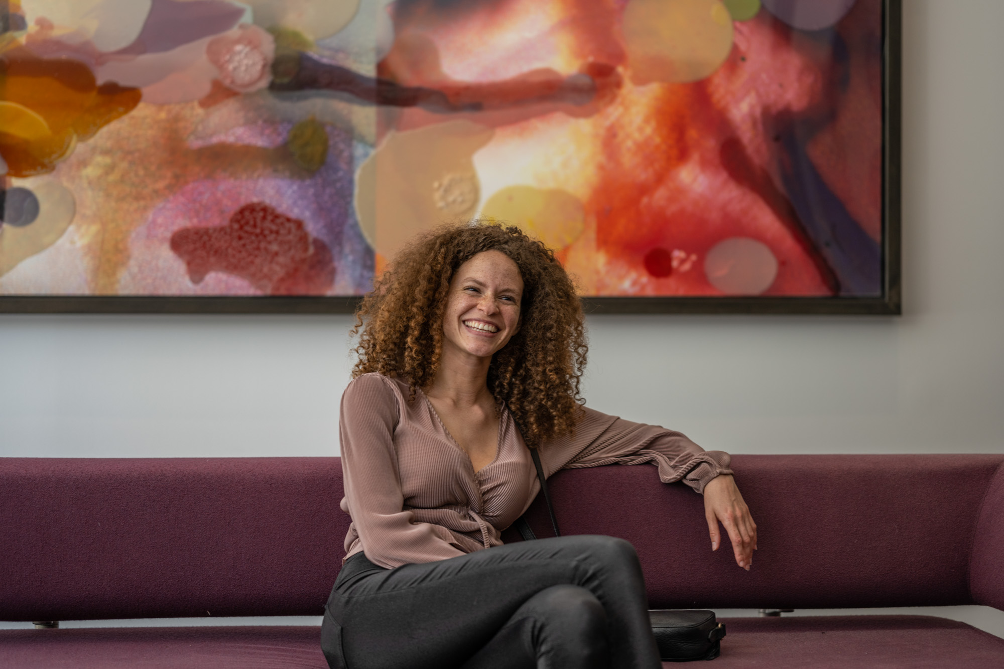 A woman smiles against colorful wall art in a common room.