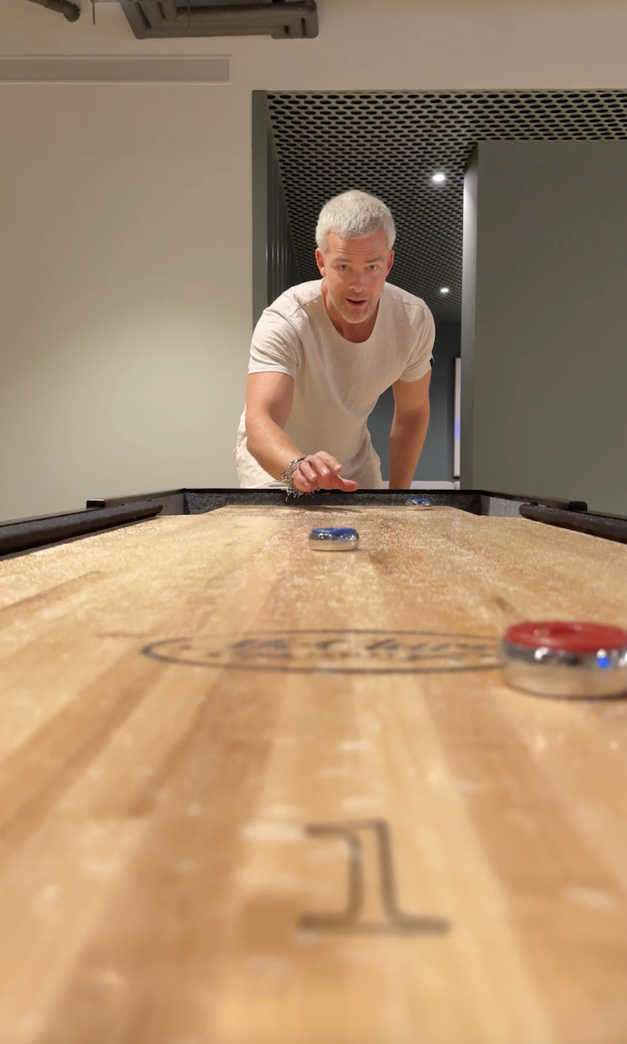 A man engaged in a game of shuffleboard inside a spacious indoor area.