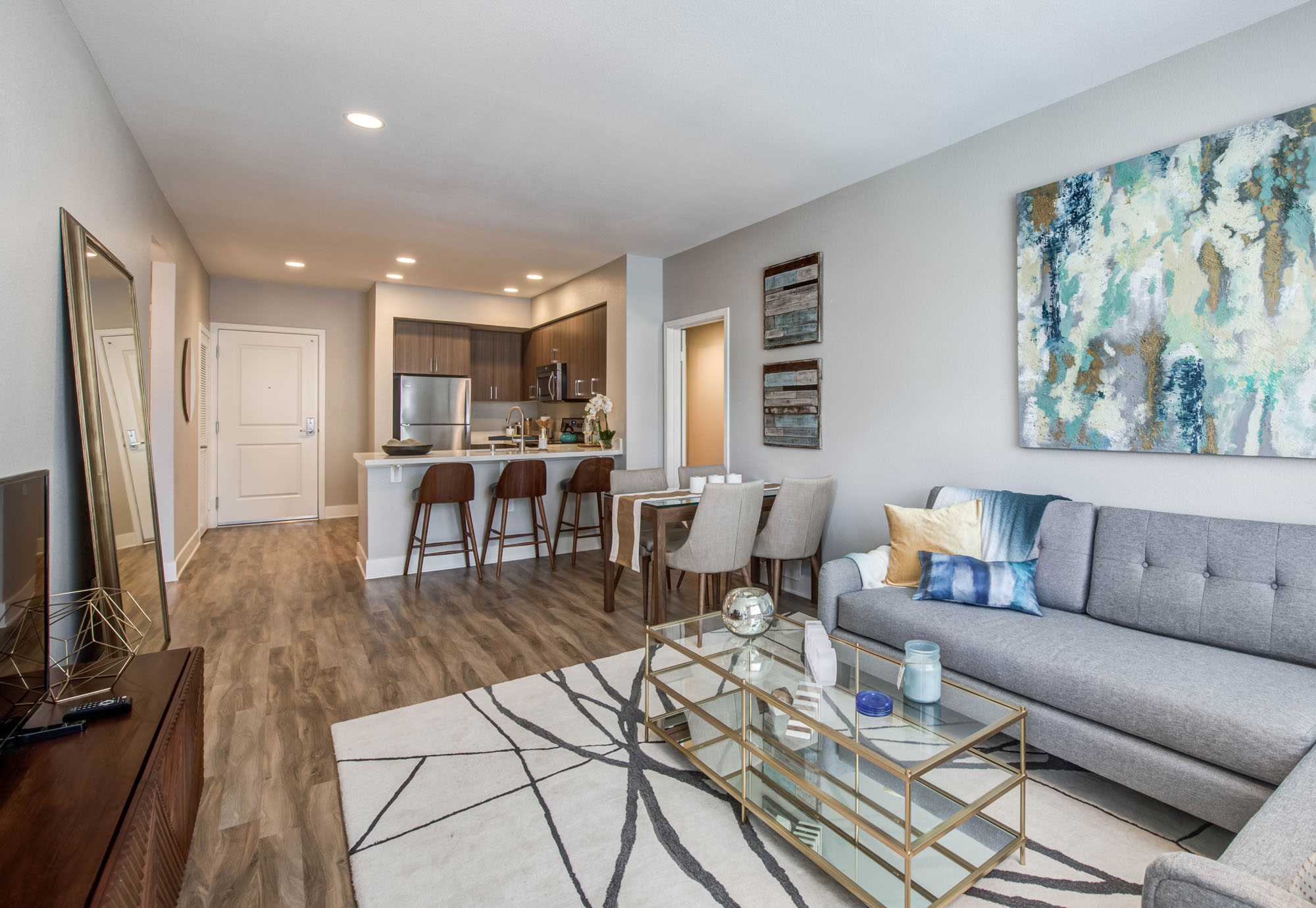 A spacious living room with wood flooring, leading into a dining space and kitchen area at Alder apartments in Northridge CA