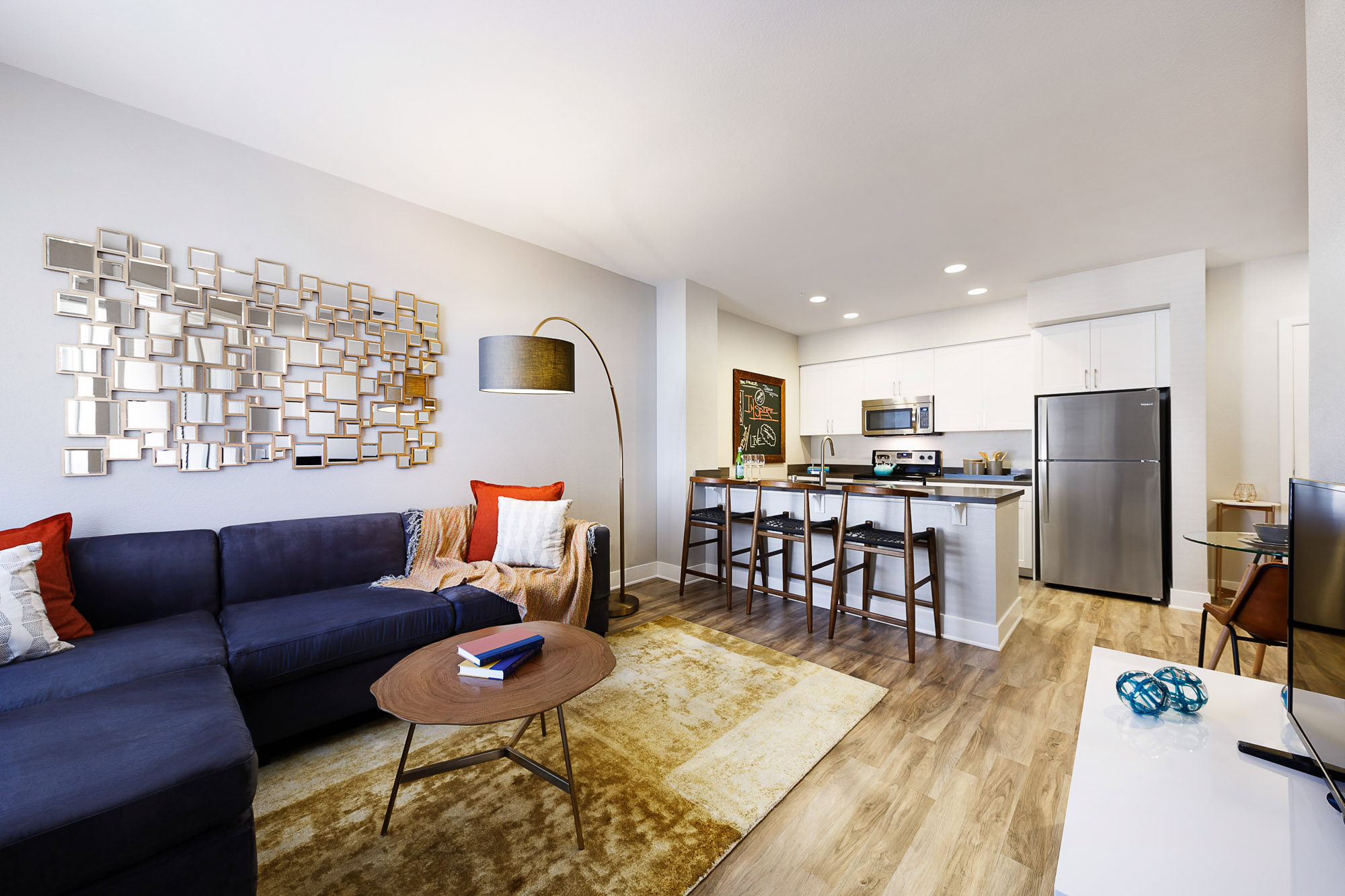 A modern living room with wood flooring leading into a kitchen at Alder apartment in Northridge California