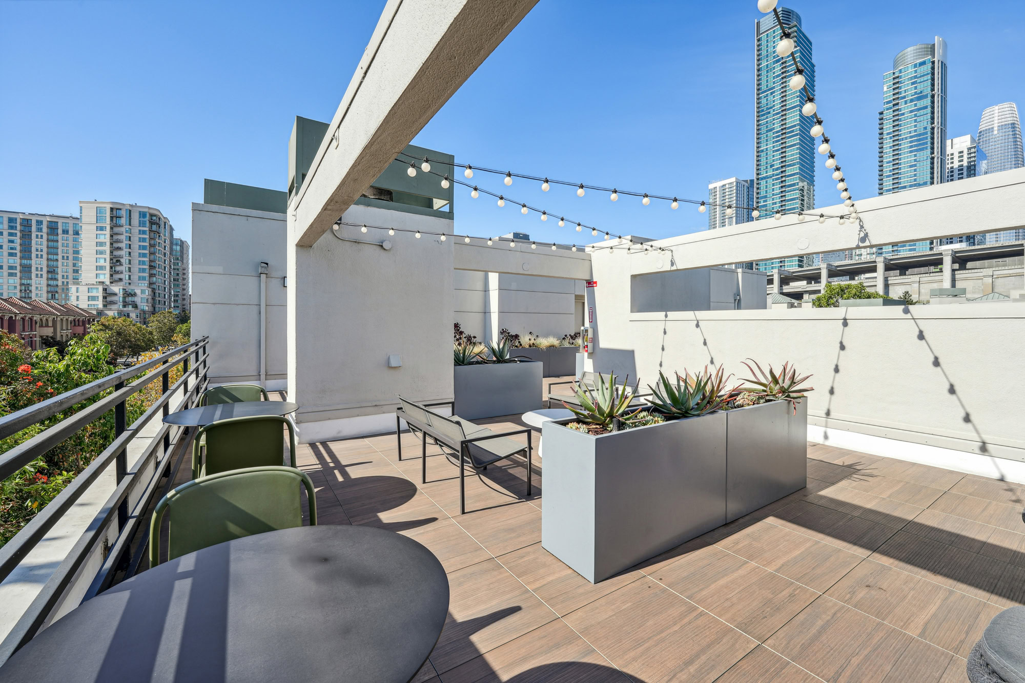 A rooftop deck with dining tables, benches, and a view of the South Park city skyline at Bayside Village apartments