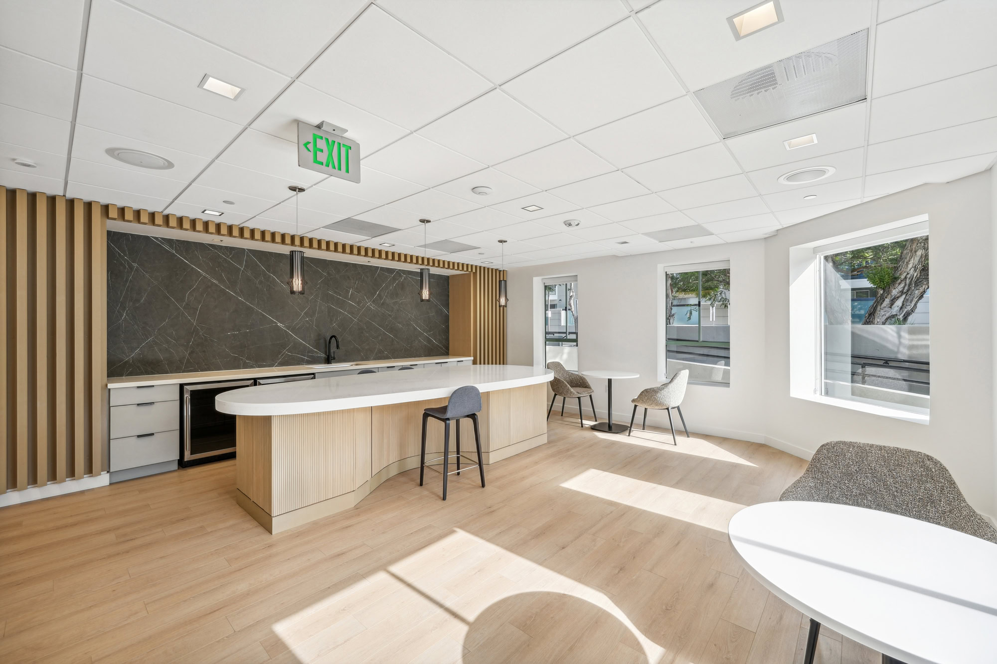 A modern fully equipped kitchen with an oval kitchen island, and several small dining tables in a lounge at Bayside Village in San Francisco