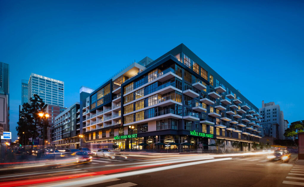 The exterior of whole foods and 8th and Grand luxury apartment building on the corner of a busy street in downtown LA