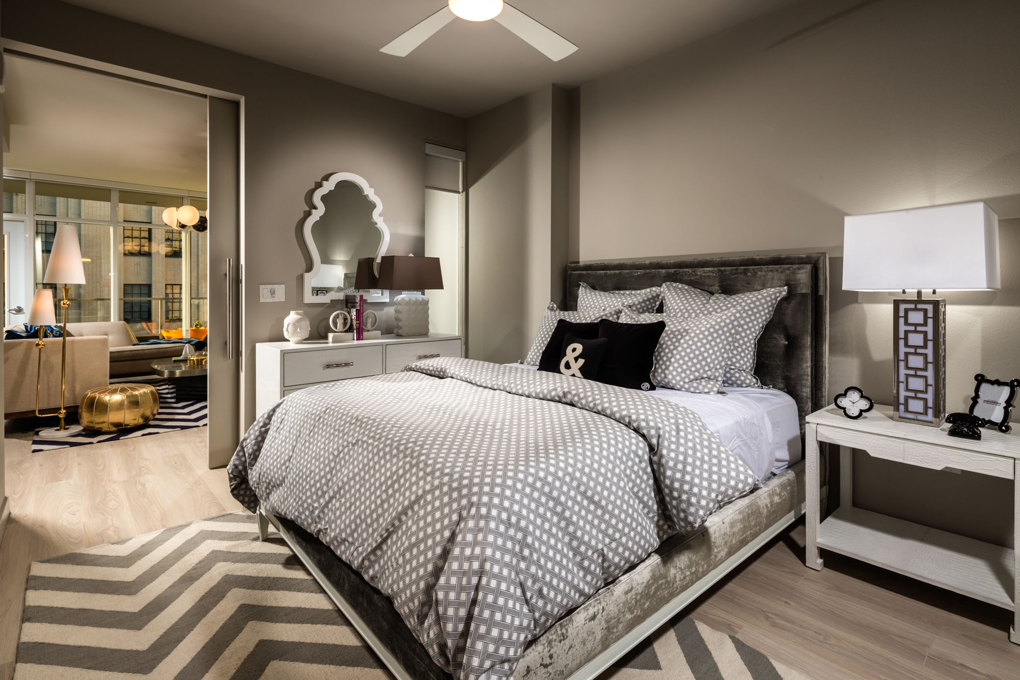 A spacious furnished bedroom with a sliding door leading to a living room space at 8th and Grands DTLA luxury apartments