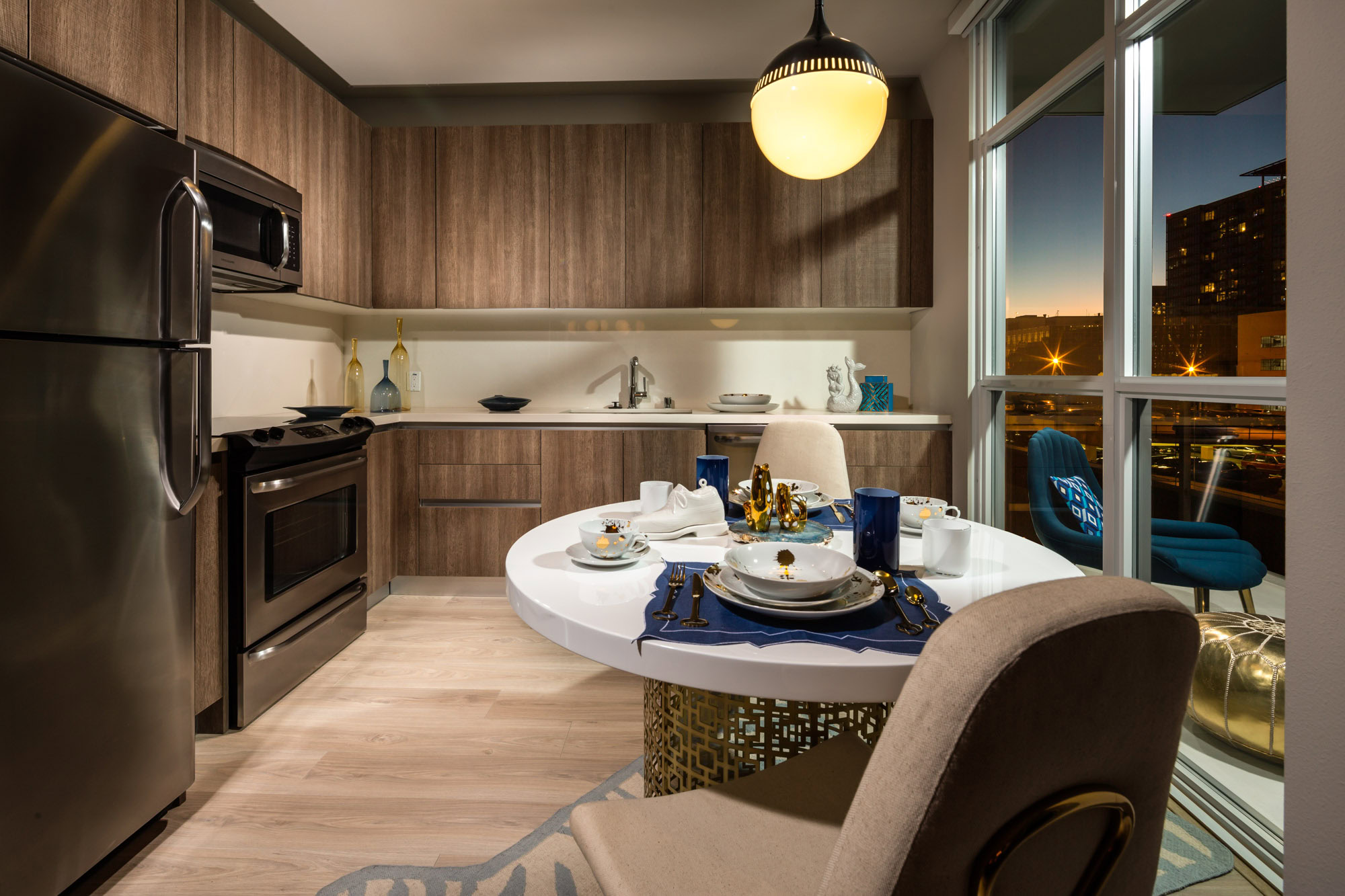 A dining area for 2 leading to an L shaped kitchen with a floor to ceiling window wall overlooking a balcony at 8th and Grand luxury apartments in DTLA