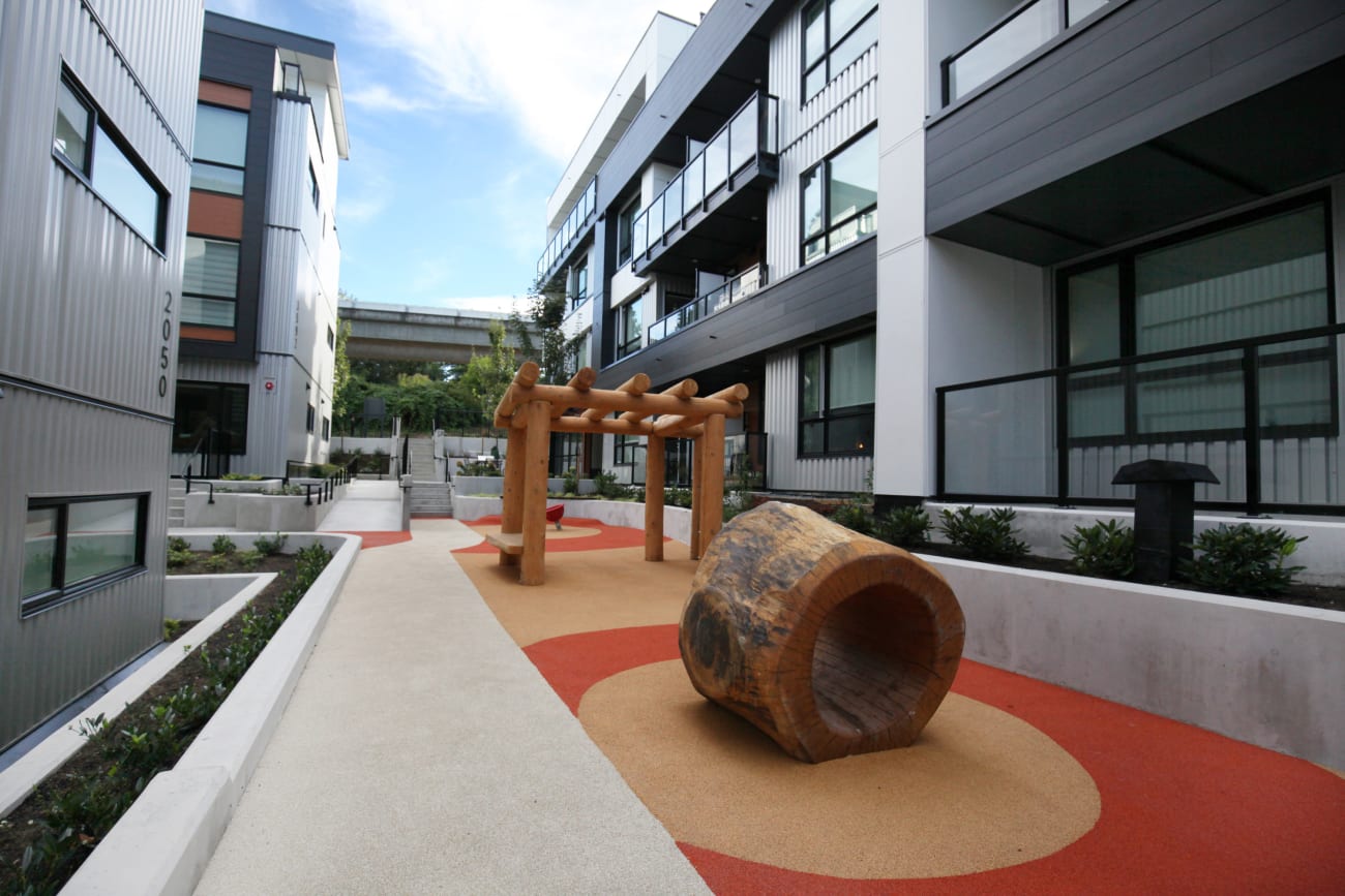 A modern courtyard with a bright orange and yellow patch, hollow log sculpture and decorative pergola at the Hendry Place luxury apartments in Vancouver