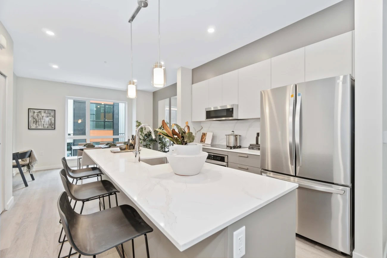 A kitchen with a kitchen island with white counters and stainless steel appliance