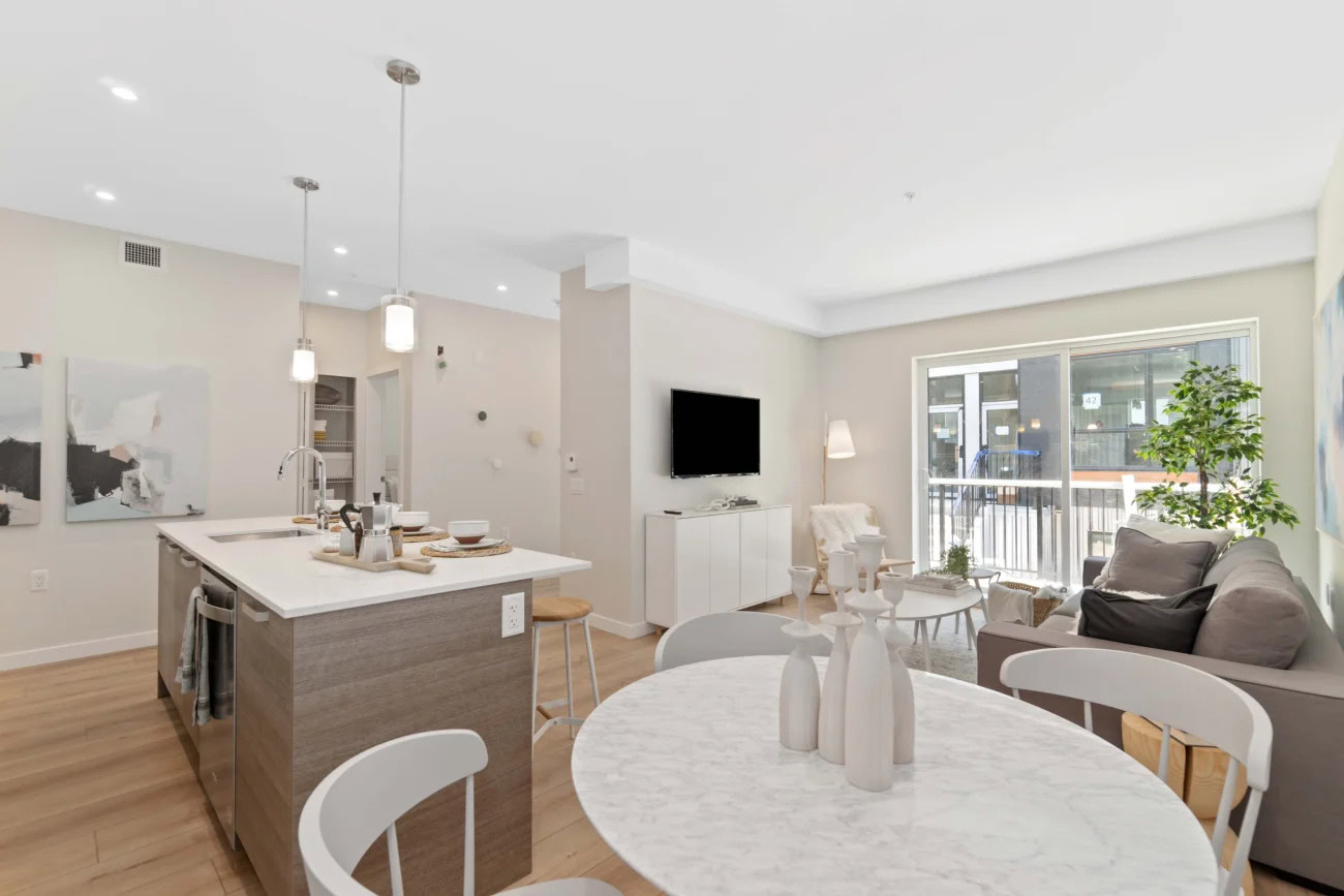An open plan dining area, kitchen Island and living room with a large glass sliding door to the balcony at the Hendry Place apartments in Vancouver