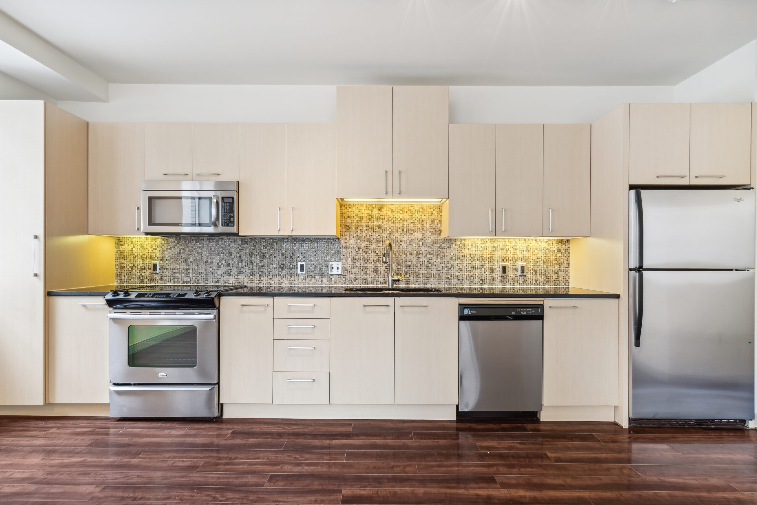 Studio kitchen with back splash, lighting, and stainless steel appliances.