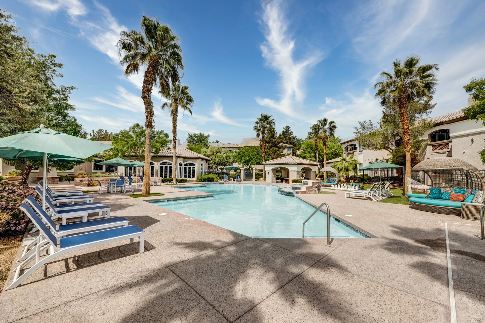 A pool with lounging chairs, umbrellas and cabana's at the Monaco Park Spring Valley apartments in Las Vegas