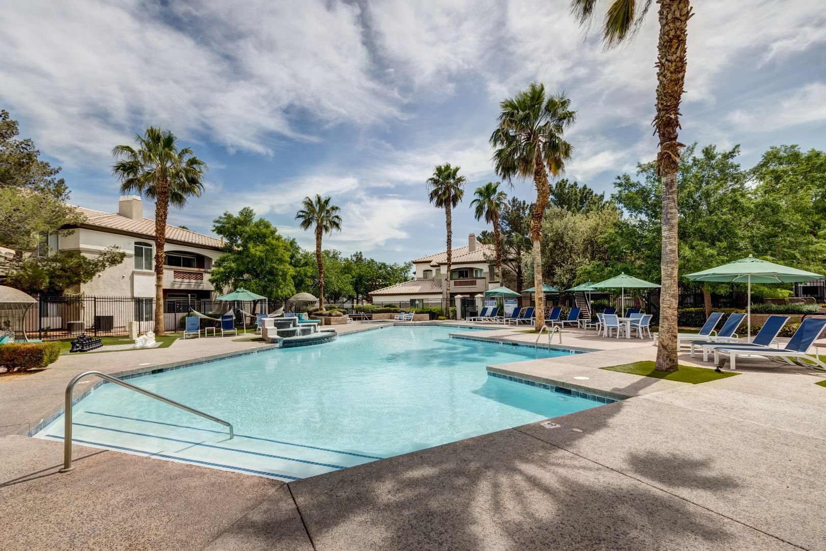 A pool with lounging chairs, umbrellas and cabana's at the Monaco Park Spring Valley apartments in Las Vegas