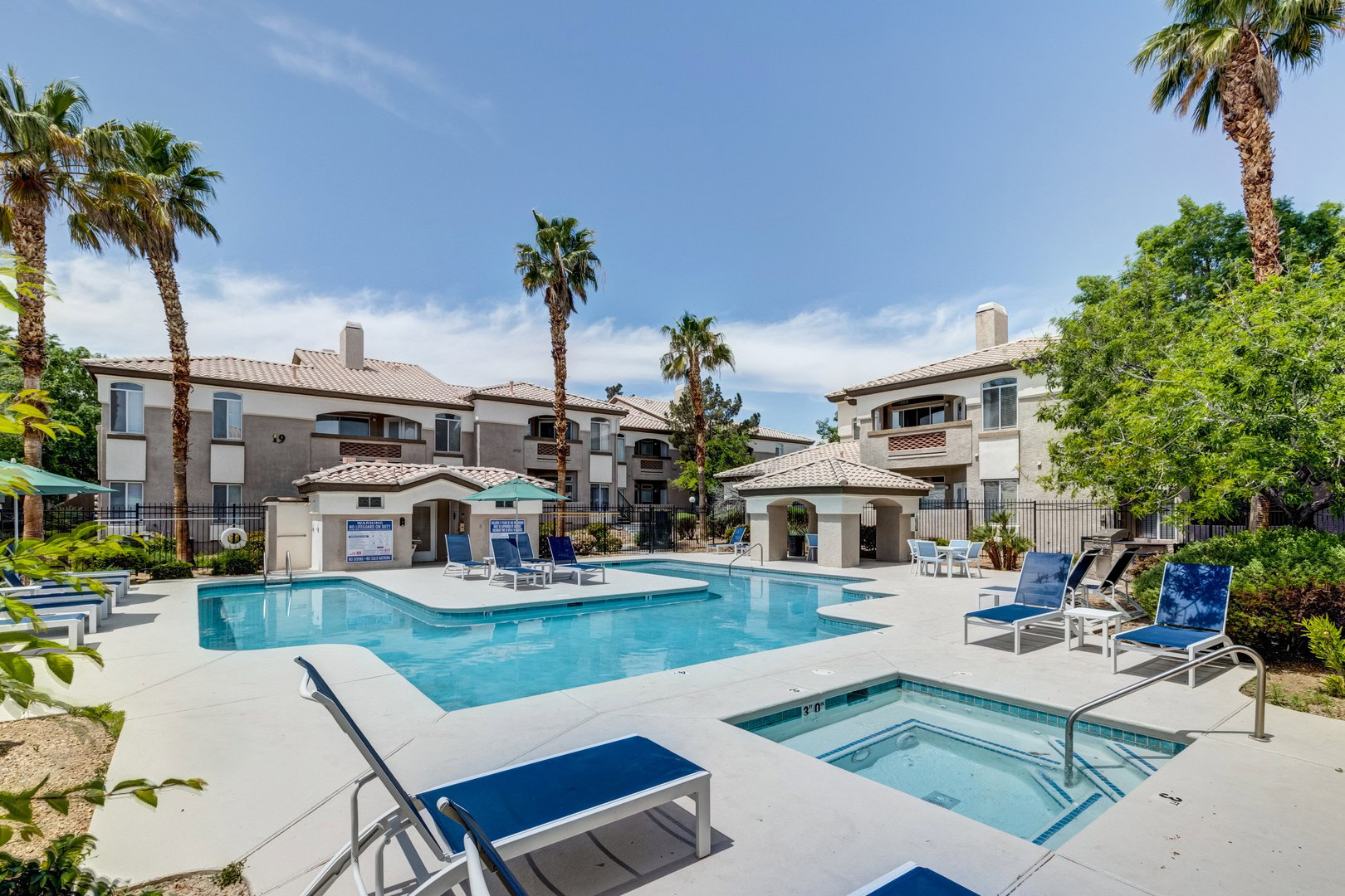 A pool area with lounging chairs and palm tree's featuring a jacuzzi and geometric pool at the Monaco Park Spring Valley apartments