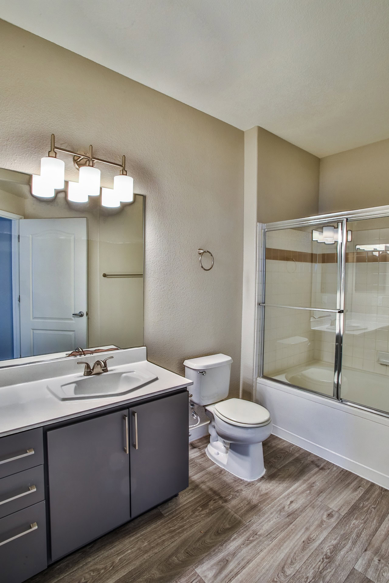 A spacious bathroom with hardwood floors, a spacious vanity and a tub and shower featuring a glass sliding door at Monaco Parks Spring Valley apartments