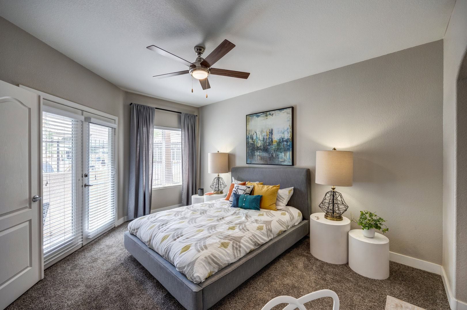 A bedroom with carpet flooring and glass double doors leading to a balcony next to a large window at the Spring Valley Monaco Park apartments