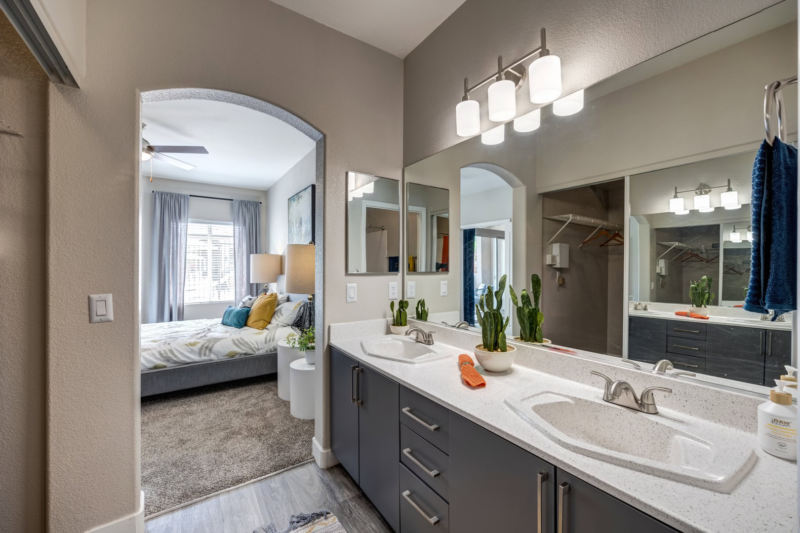 An ensuite carpeted bedroom seen from a bathroom with a closet featuring a his and hers vanity sink at Monaco Park Las Vegas apartment