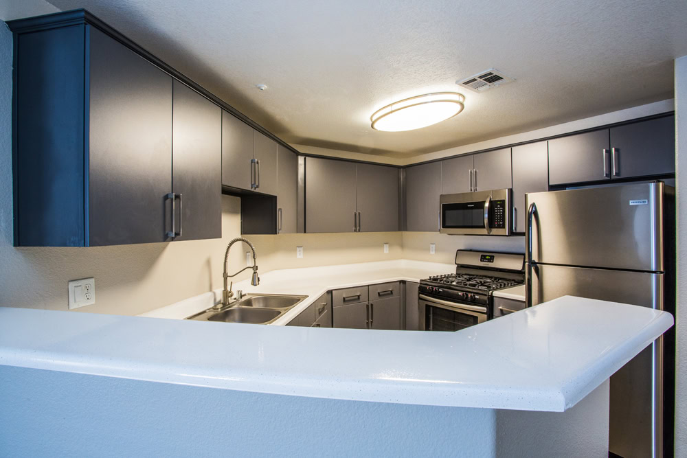 A kitchen with stainless steel appliances and a high kitchen counter overlooking the living room at Monaco Parks Spring Valley apartments