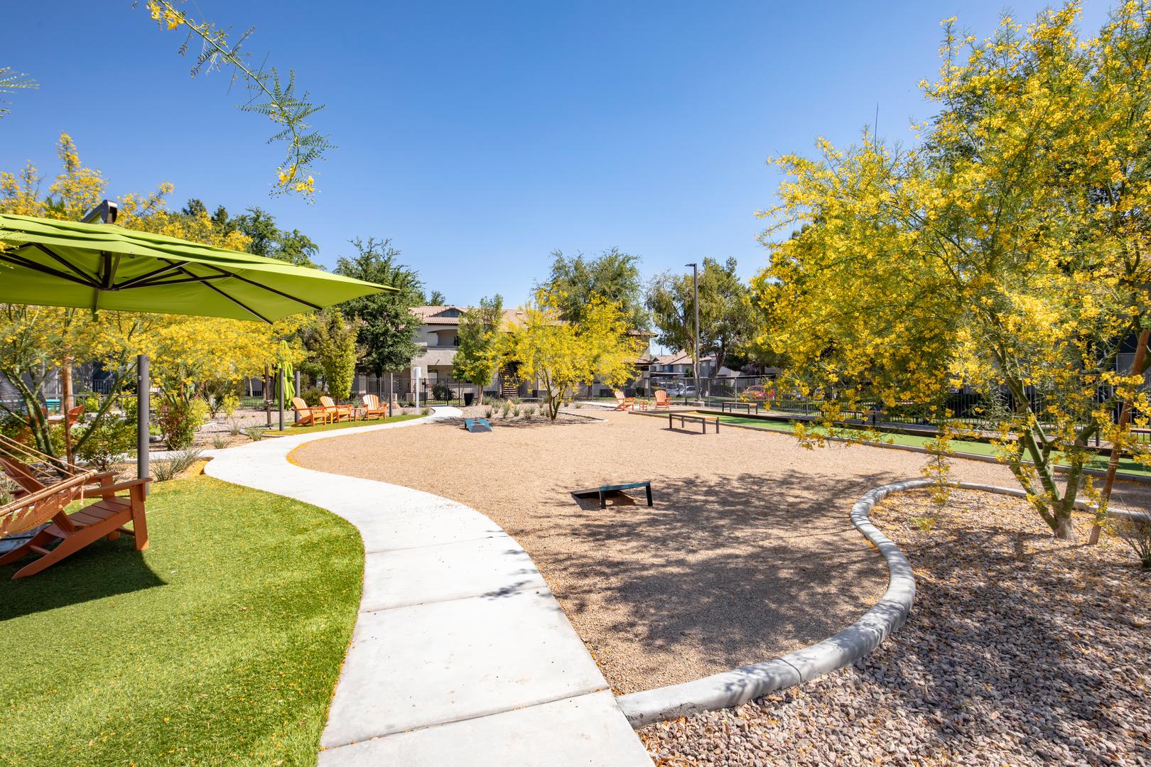 An outdoor recreational space with cornhold games, lounging chairs and a path between the grass at Xander 3900 apartments in Las Vegas
