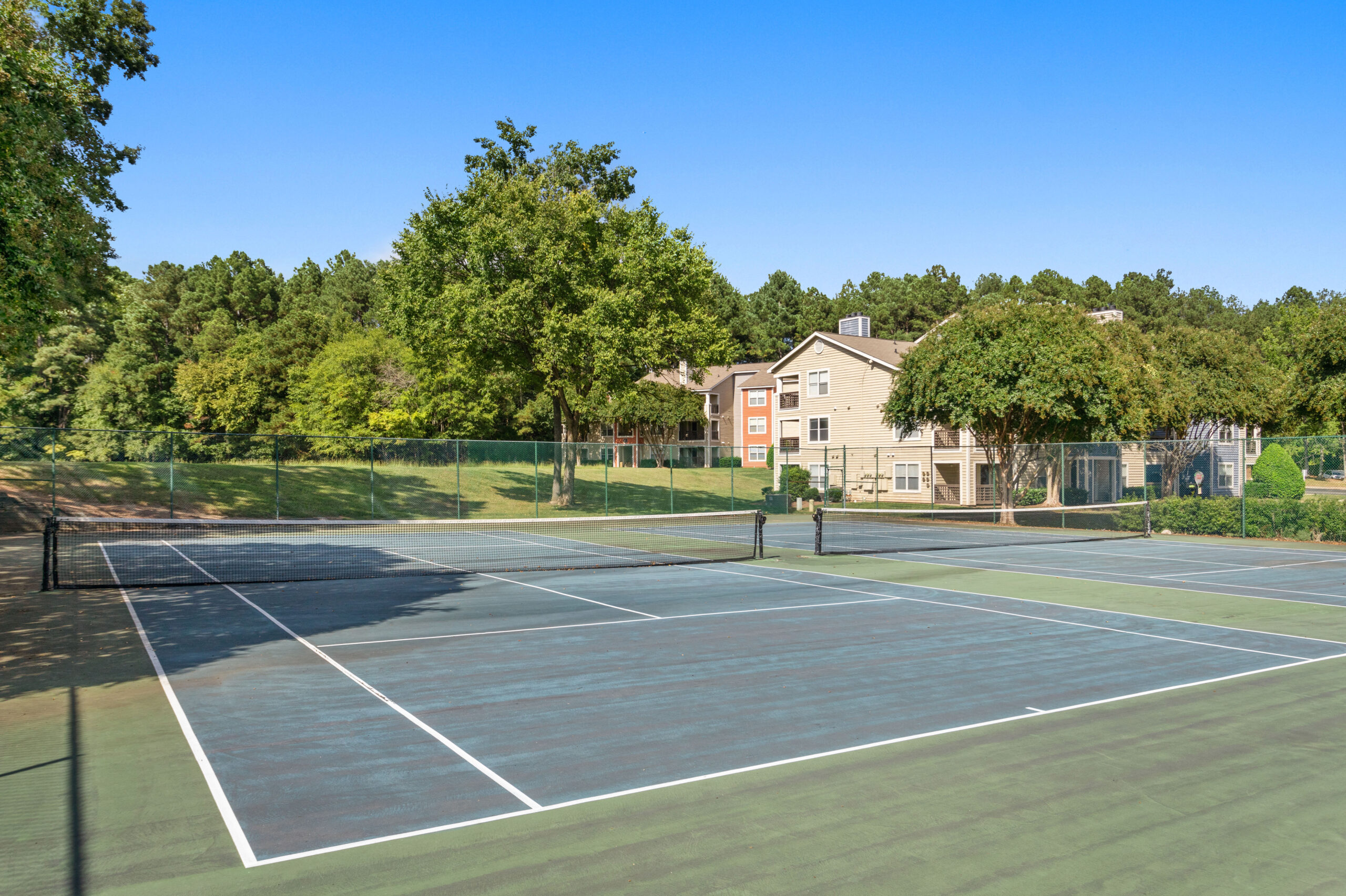 Two tennis courts with trees and apartment building in the background.