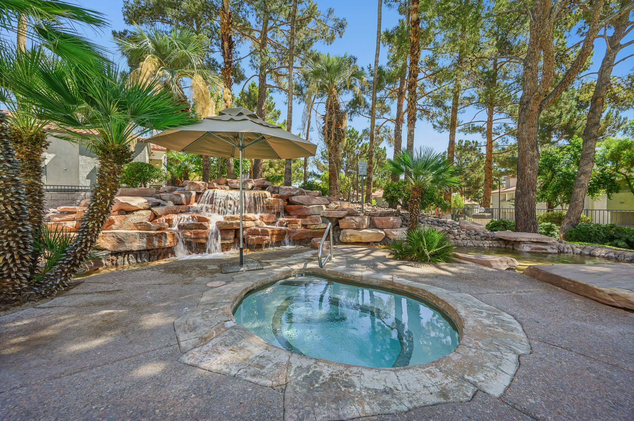 Outdoor hot tub at Vintage Pointe surrounded by palm trees, mature landscaping, and a rock waterfall.