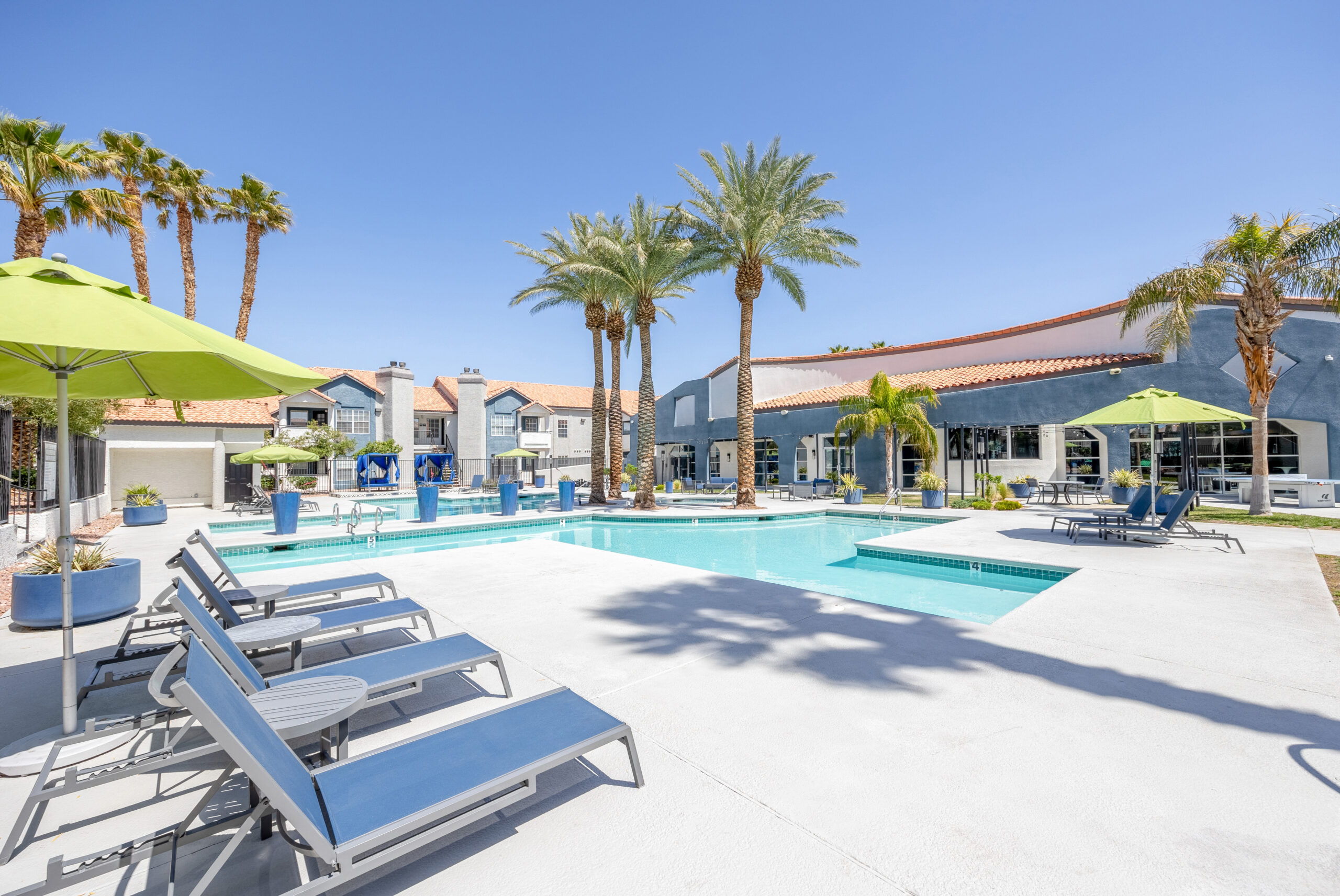A resort-style pool area with blue lounging chairs, green umbrellas and palm trees chairs at The Met Las Vegas apartments for rent
