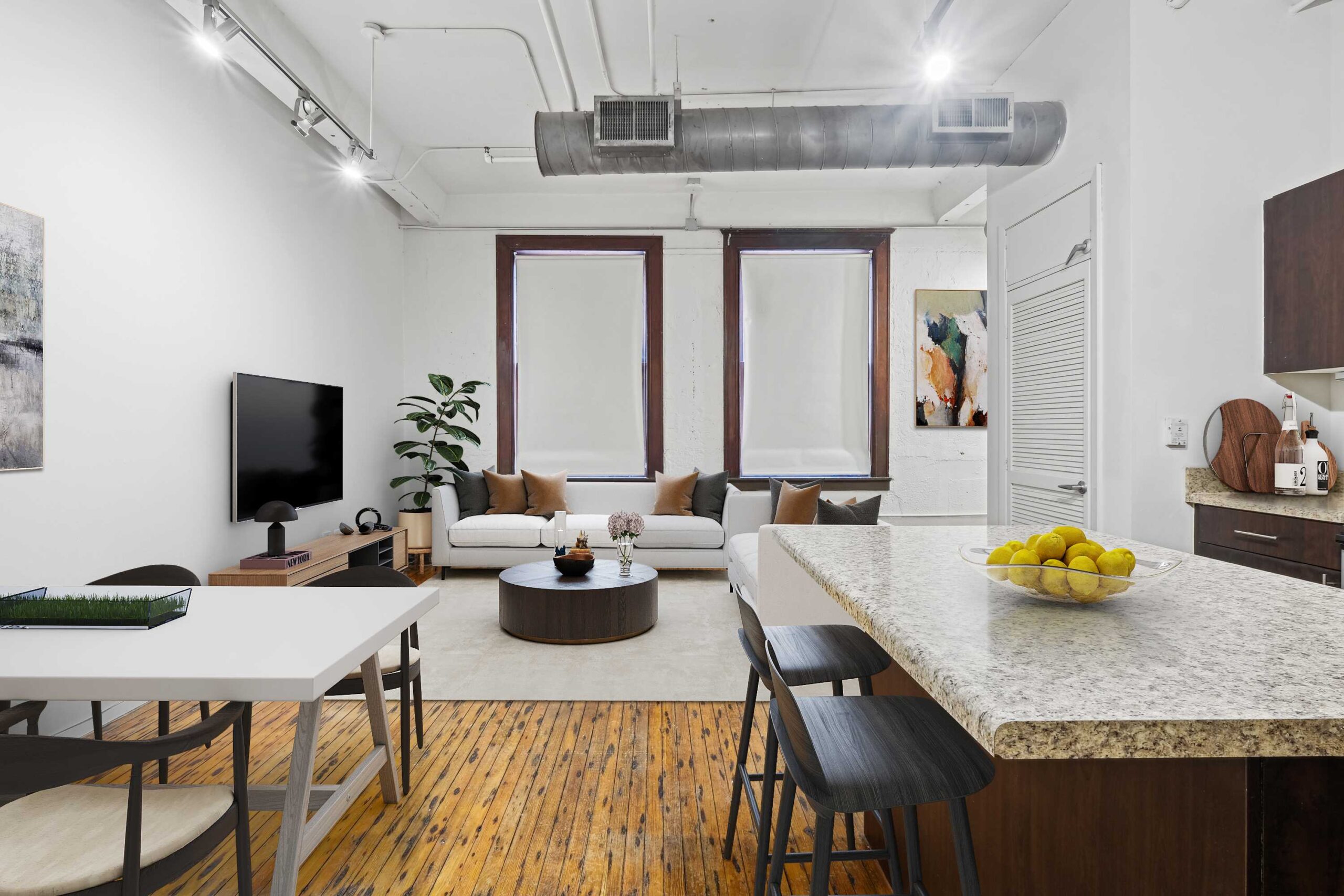 Kitchen island with stools, dining room table, hardwood floors, and industrial-style piping.