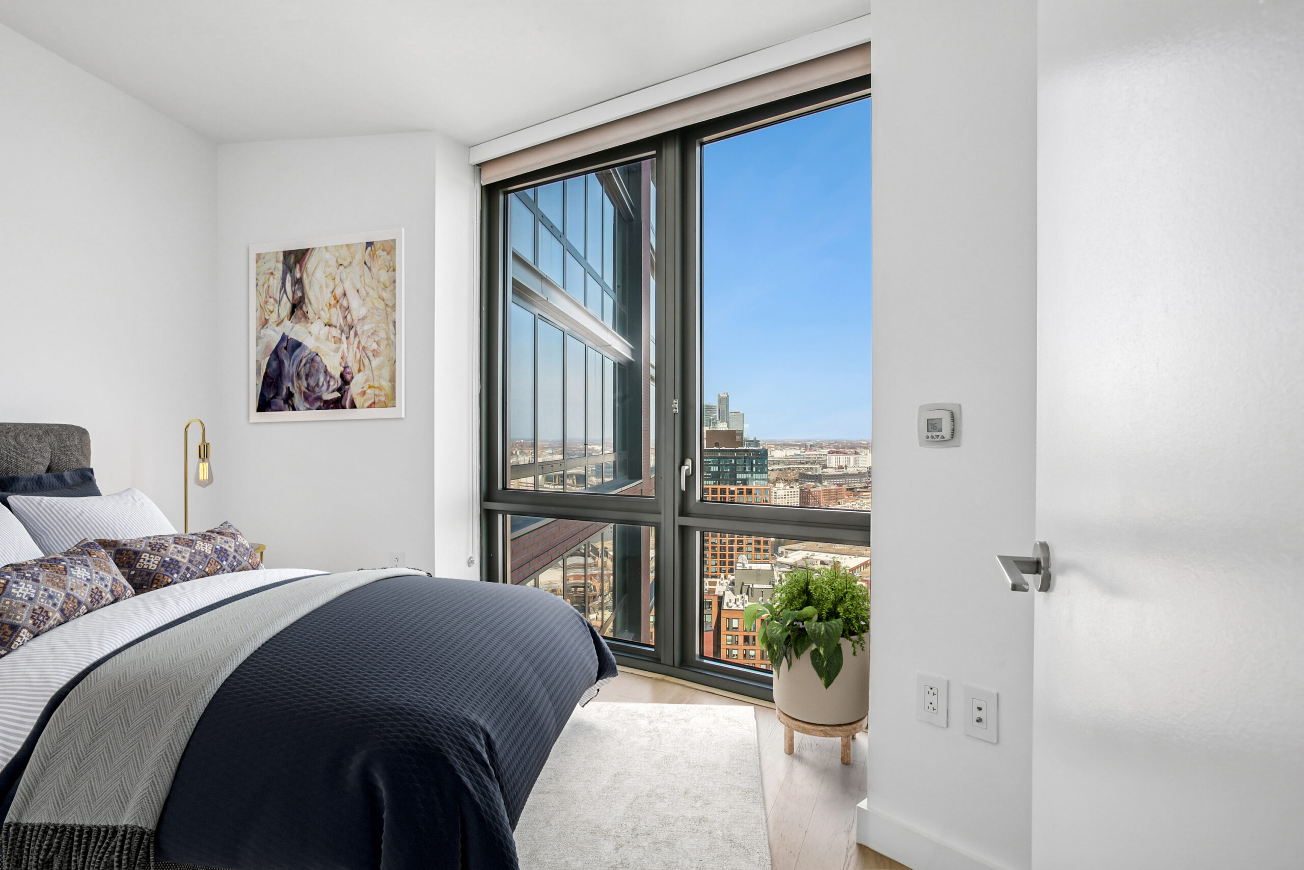 Modern bedroom with generous floor-to-ceiling windows offering city views