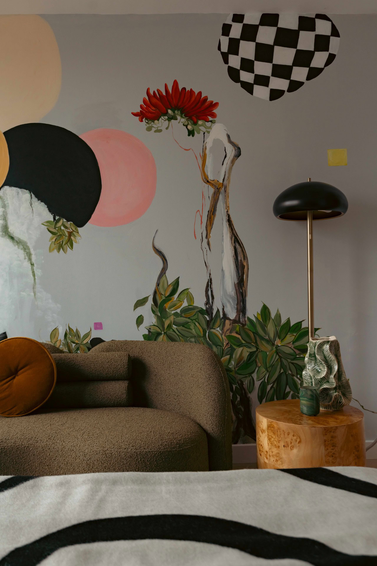A living room with a couch, a lamp and a wall mural.