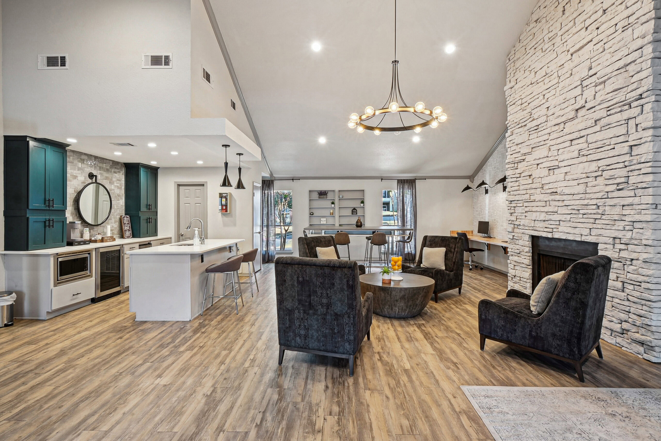 Resident clubhouse at the Arbors of Las Colinas apartment in Garland Texas featuring a modern lounge area, stone fireplace, stylish seating, and a kitchen