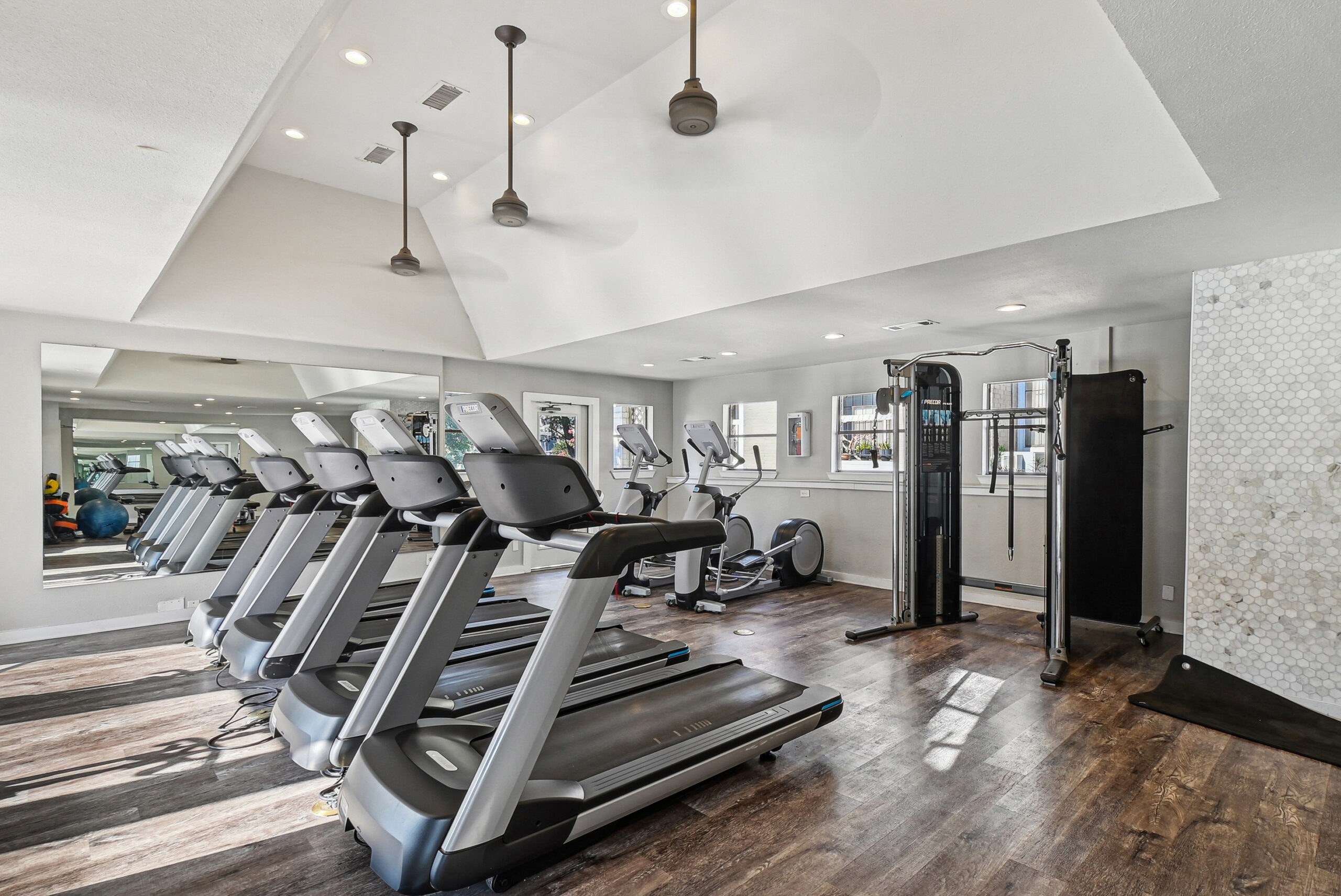 A fitness center in the Arbors of Las Colinas apartment building in Garland Texas, featuring a row of treadmills, elliptical machines and a smith machine