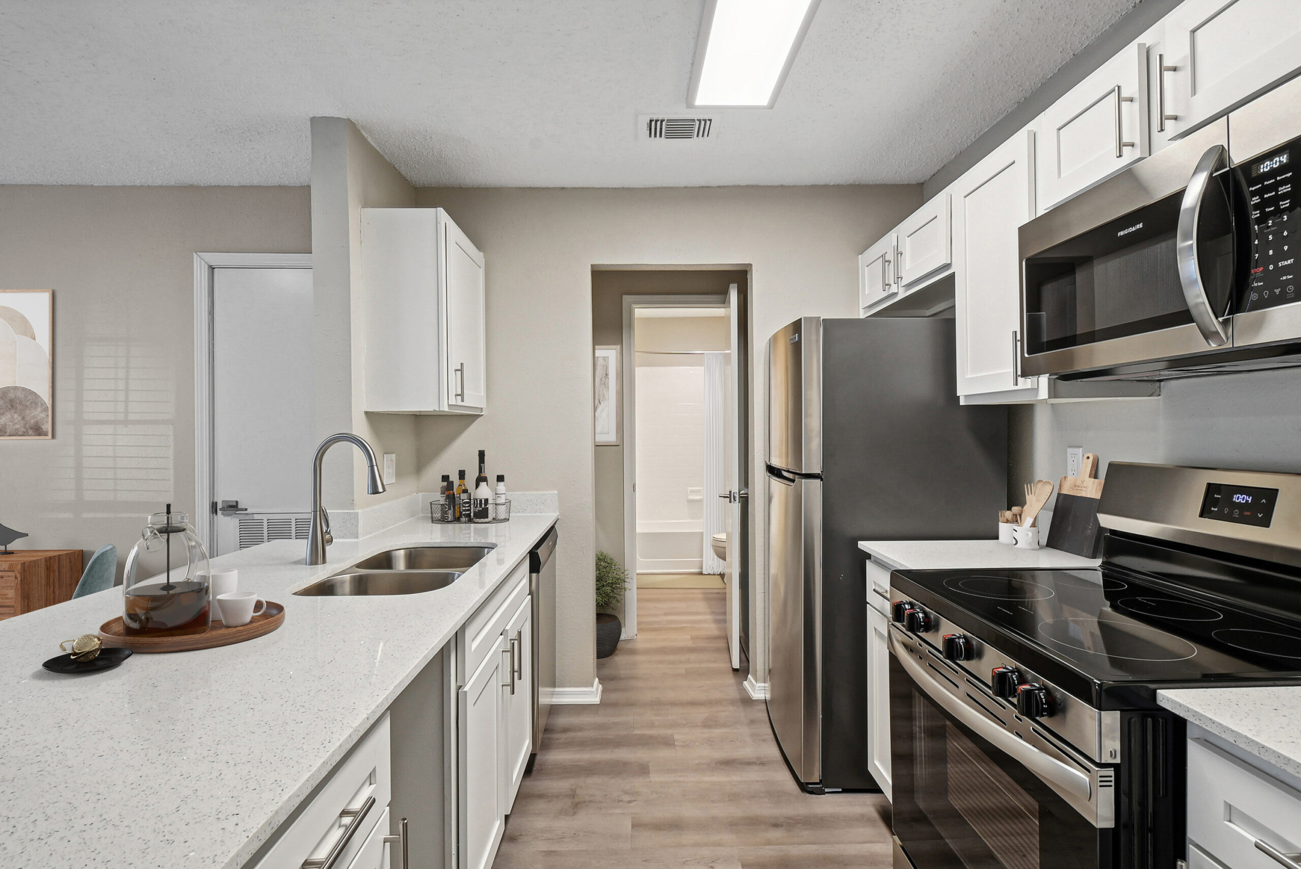 Modern apartment kitchen in Garland Texas featuring white cabinets, stainless steel appliances, and quartz style countertops.