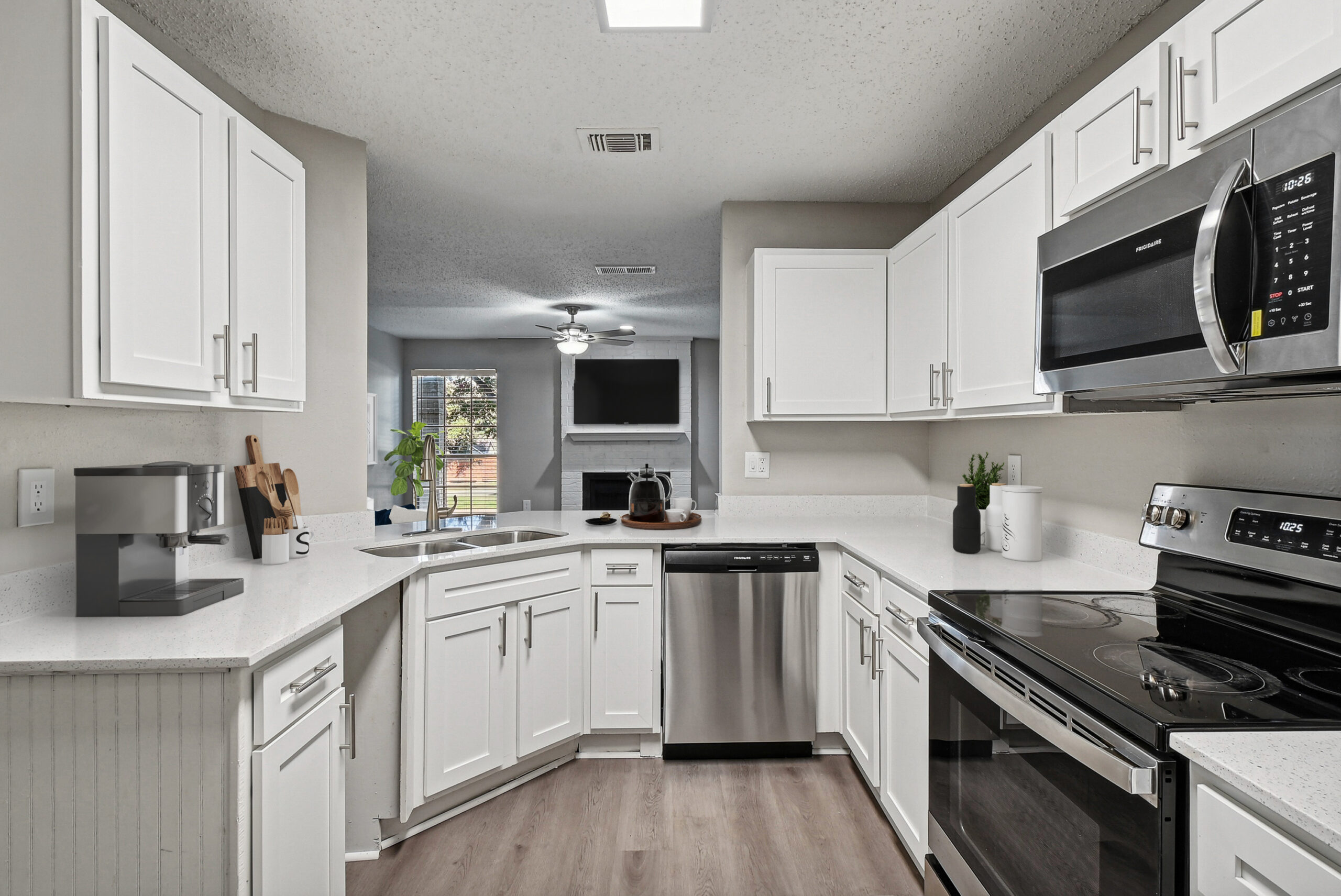 Modern U-shaped apartment kitchen in Garland Texas, featuring white cabinets, stainless steel appliances, and white marble countertops.
