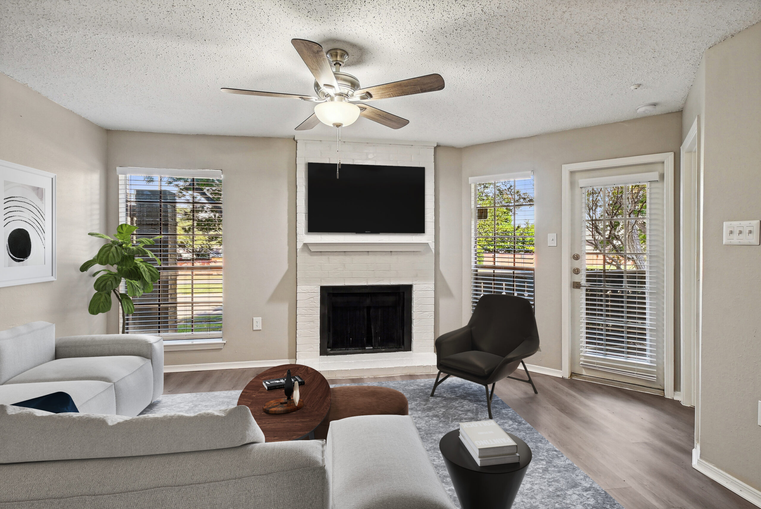 A Modern living room apartment in Garland Texas, featuring a white brick fireplace, large windows, and wood-style floors.
