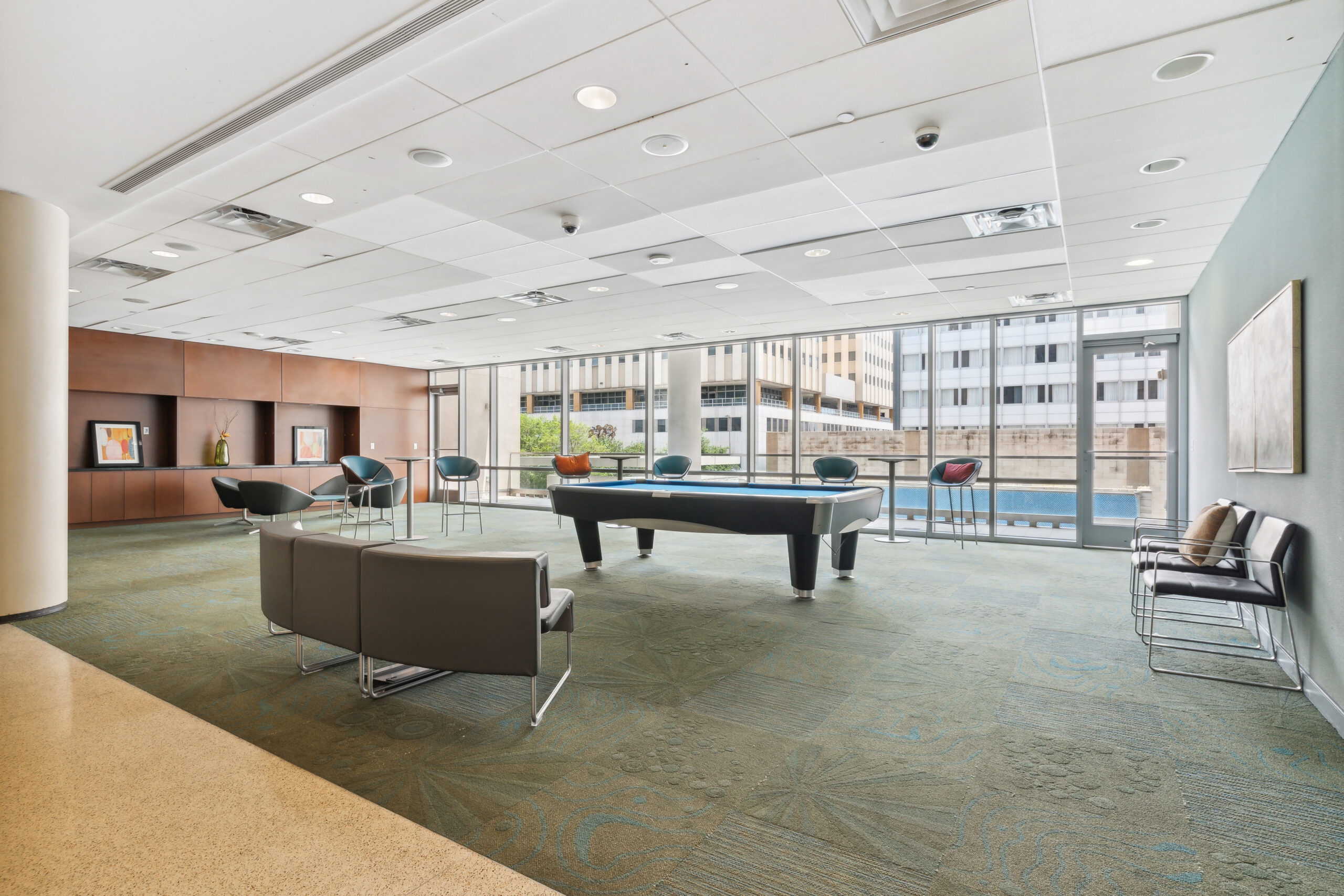 A lounge with seating, a pool table in the middle, high tables and a floor to ceiling window wall at The Continental apartments in Dallas, Texas