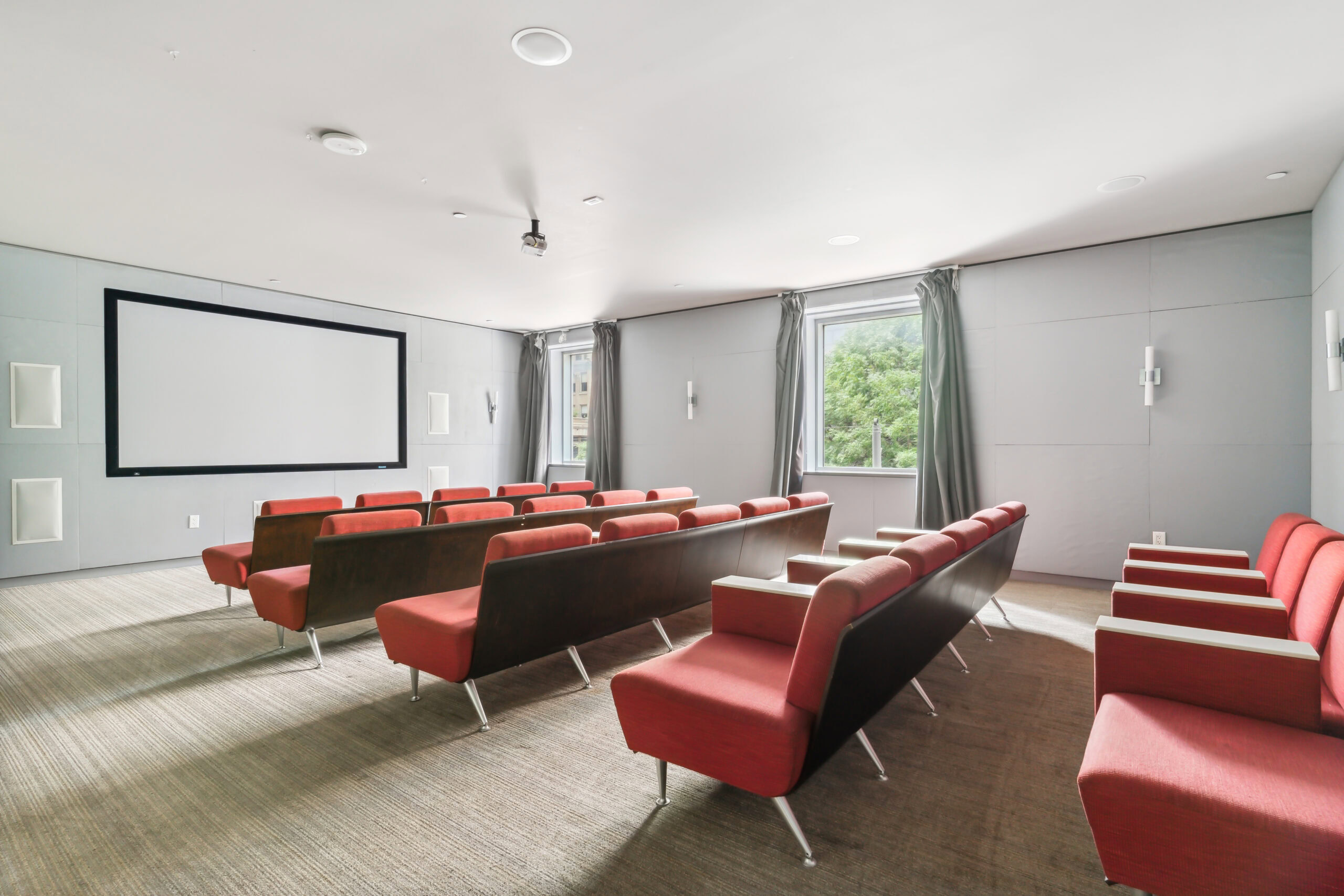 A movie theatre at The Continental housing apartments with rows of conjoined seats, and two windows with curtains