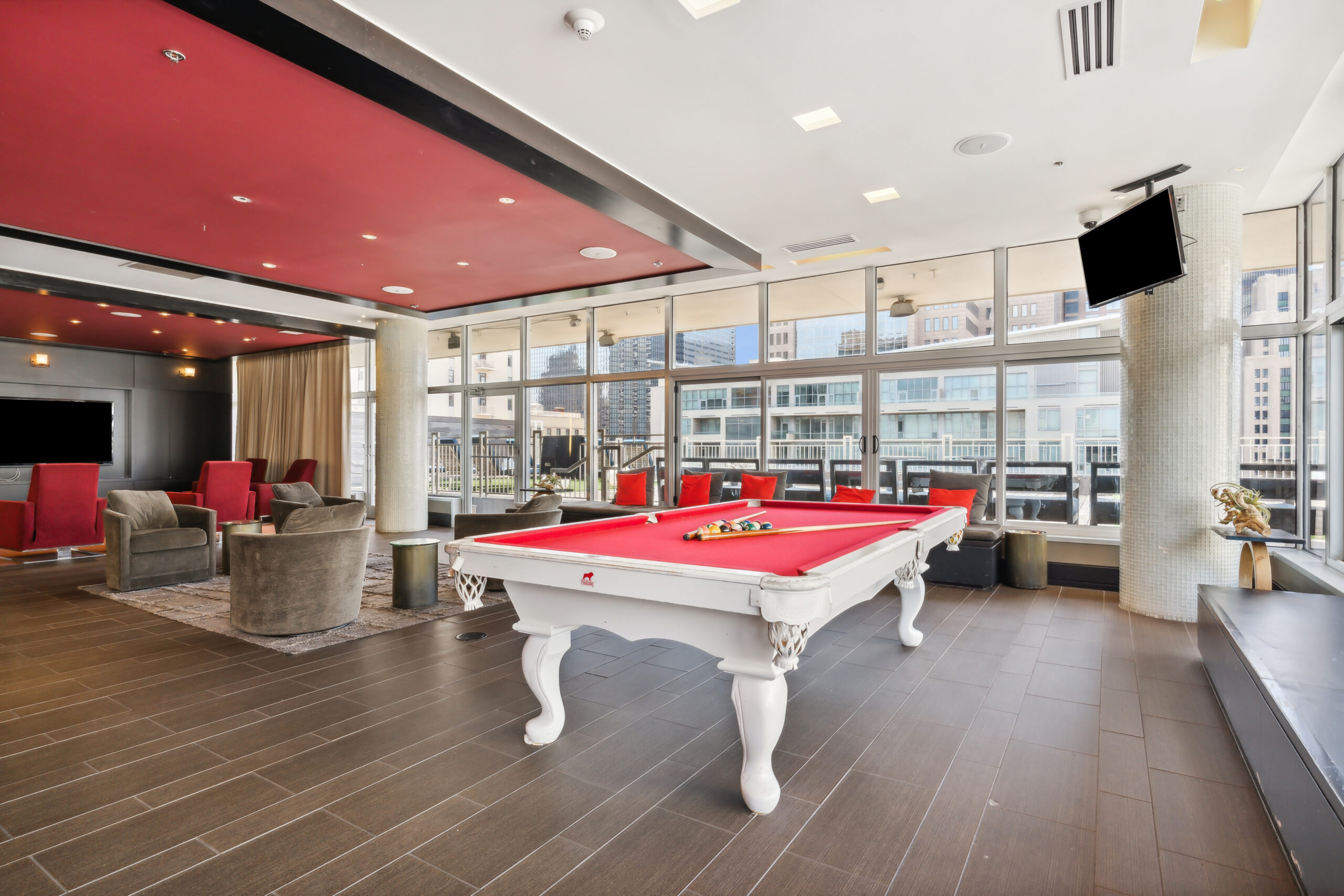A white and red pool table in the rooftop lounge at The Continentals apartments with large windows offering a city view and natural lighting