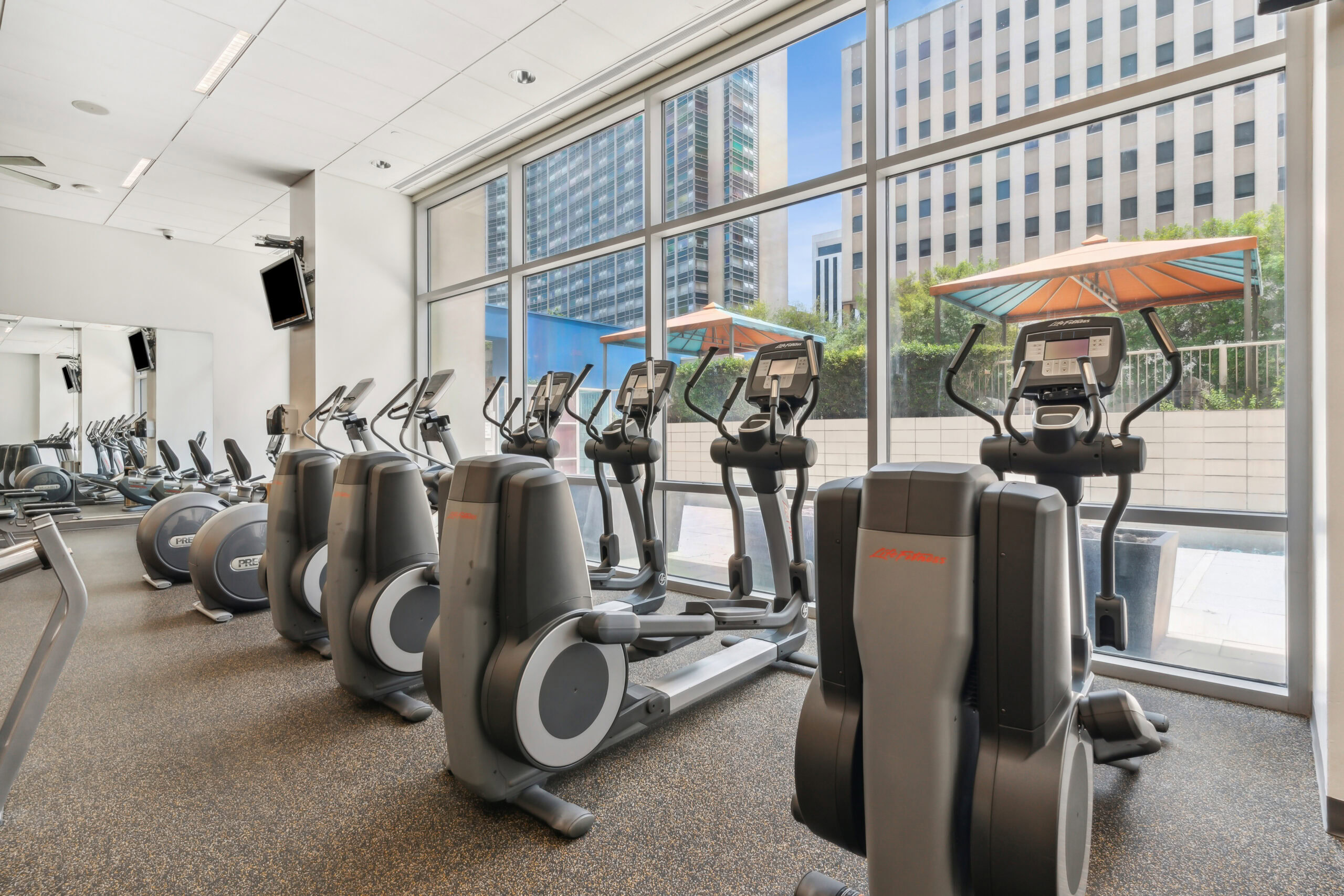 A fitness center with elliptical machines lined against the window wall at The Elements apartments in Dallas Texas