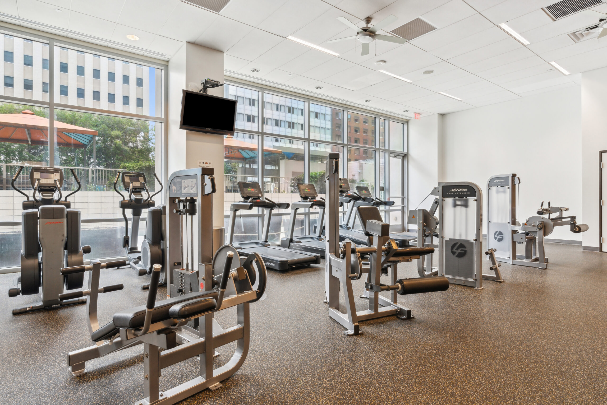 A fitness center with treadmills, ellipticals and weight machines facing a window wall at The Element apartments in Dallas Texas