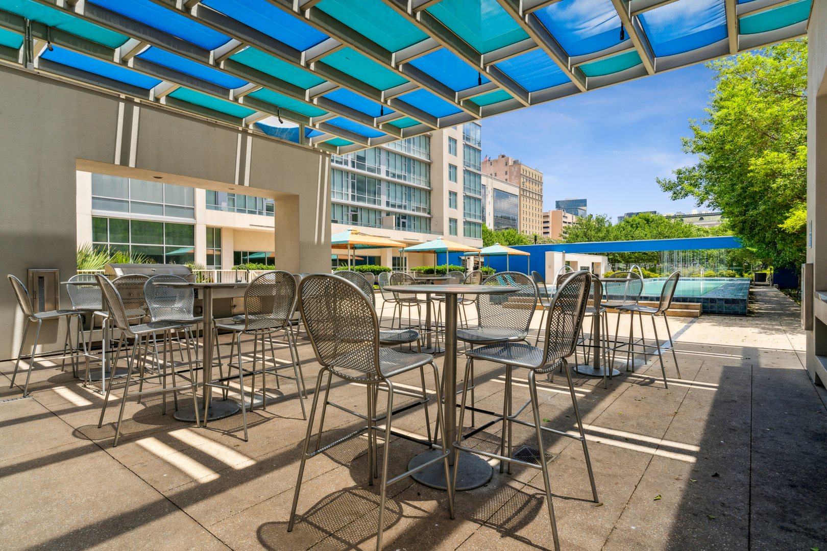 Outdoor high tables and chairs under blue glass run roof at The Elements luxury apartments in Dallas Texas
