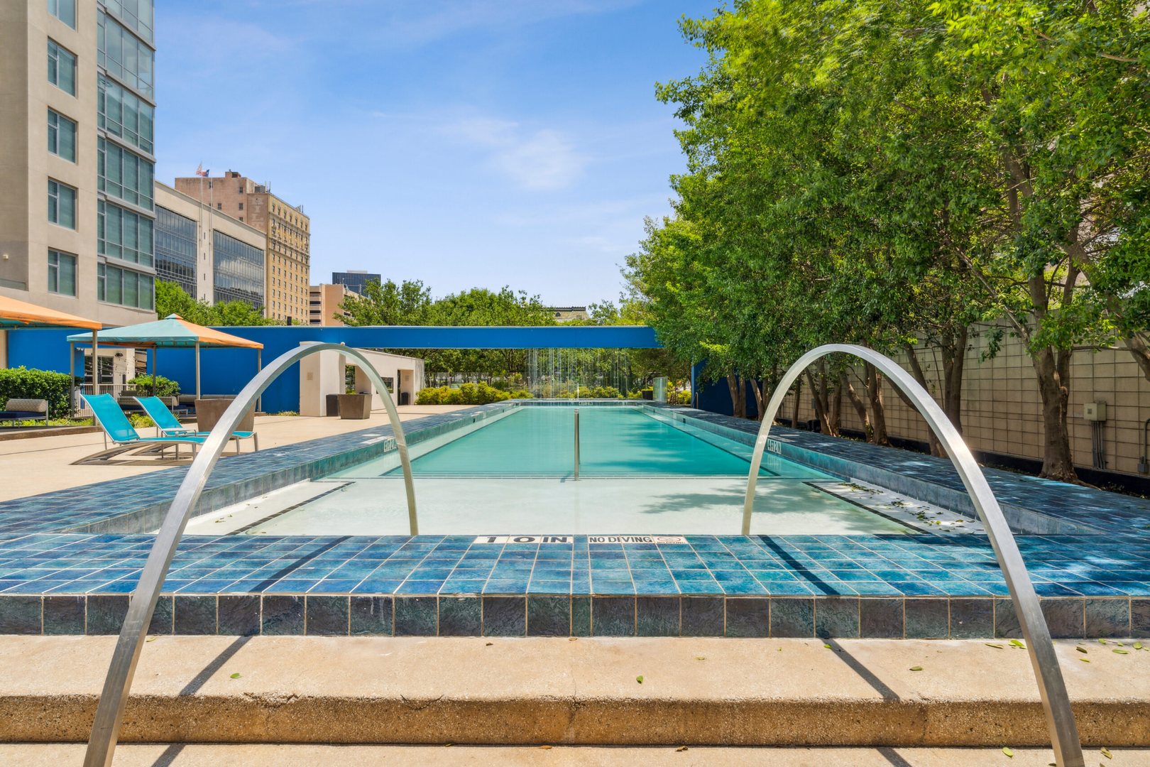 A pool with blue tile deck, blue lounging chairs and trees for privacy surrounded at The Element apartments in Dallas Texas