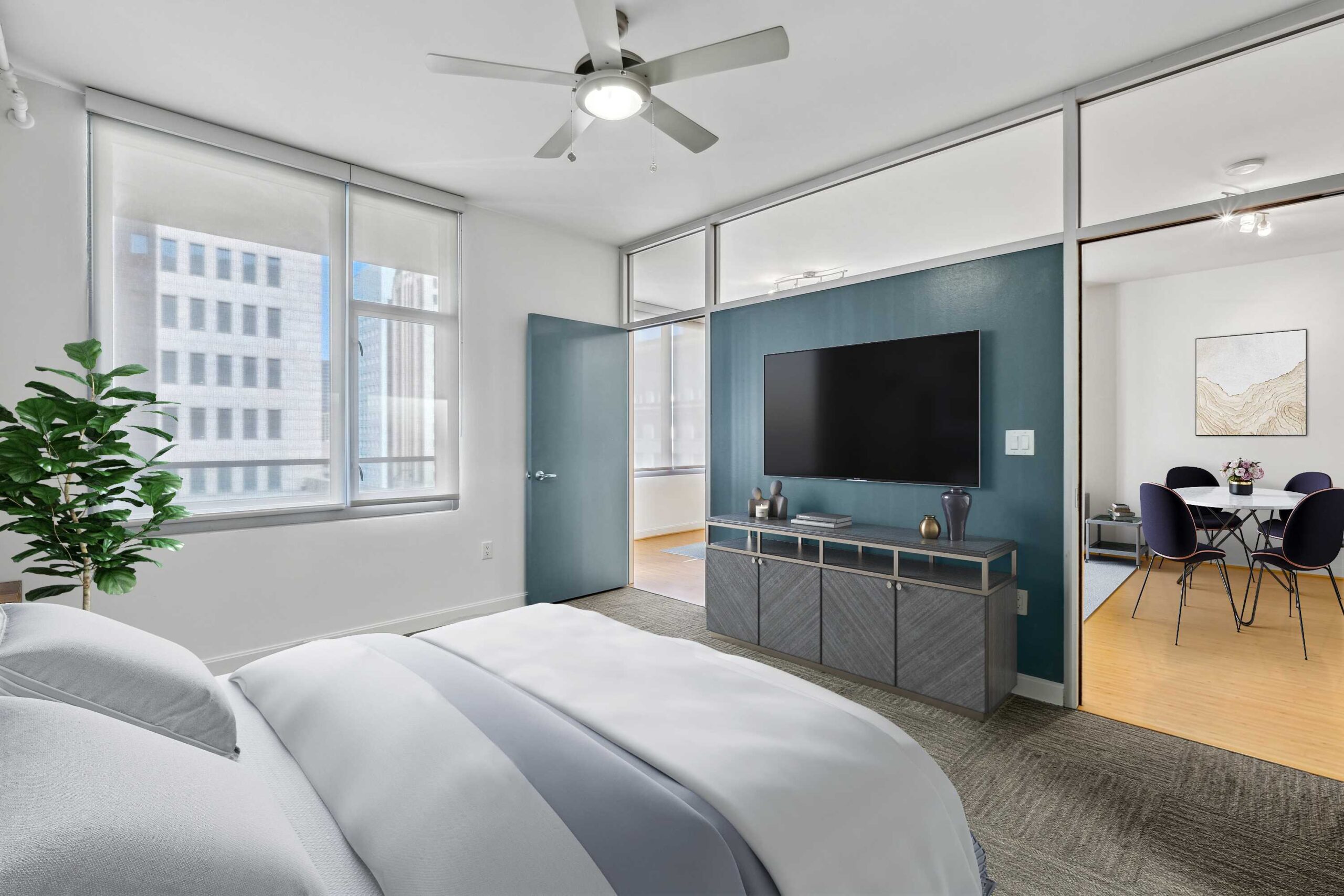 A modern apartment bedroom with a glass wall at the top and two doors facing the dining and living room area at The Elements luxury apartments in Downtown Dallas