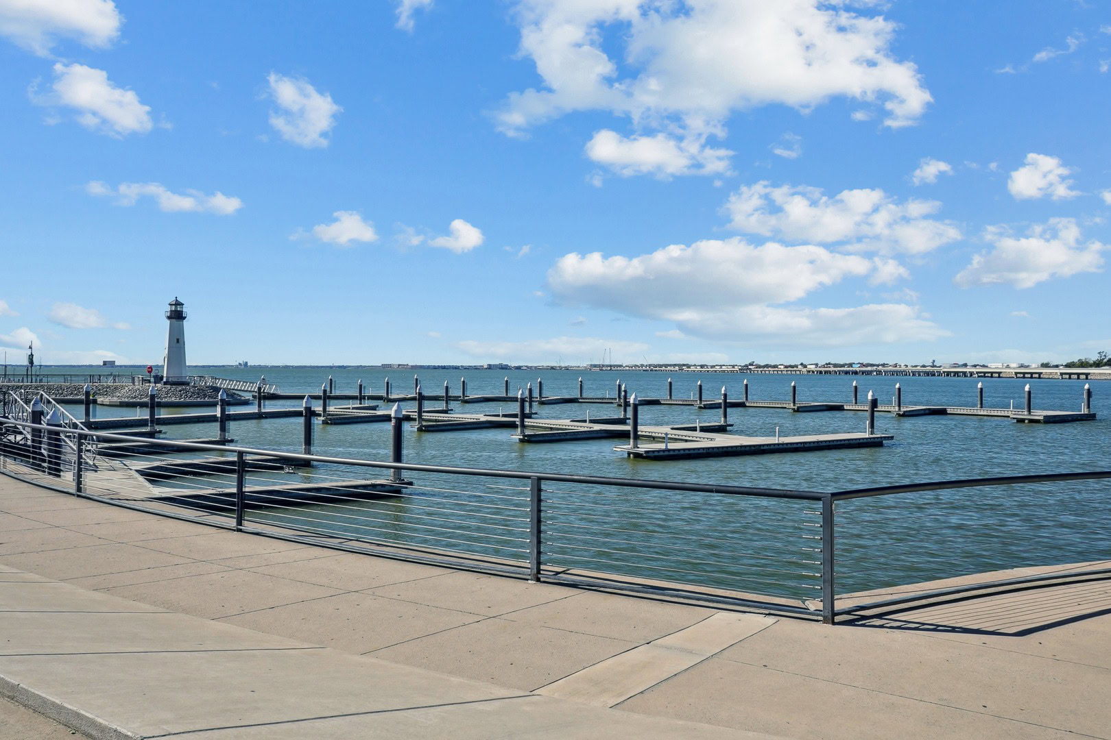Waterfront marina with empty boat slips and a lighthouse under a bright blue sky near Embree Hill apartments in Garland, Texas