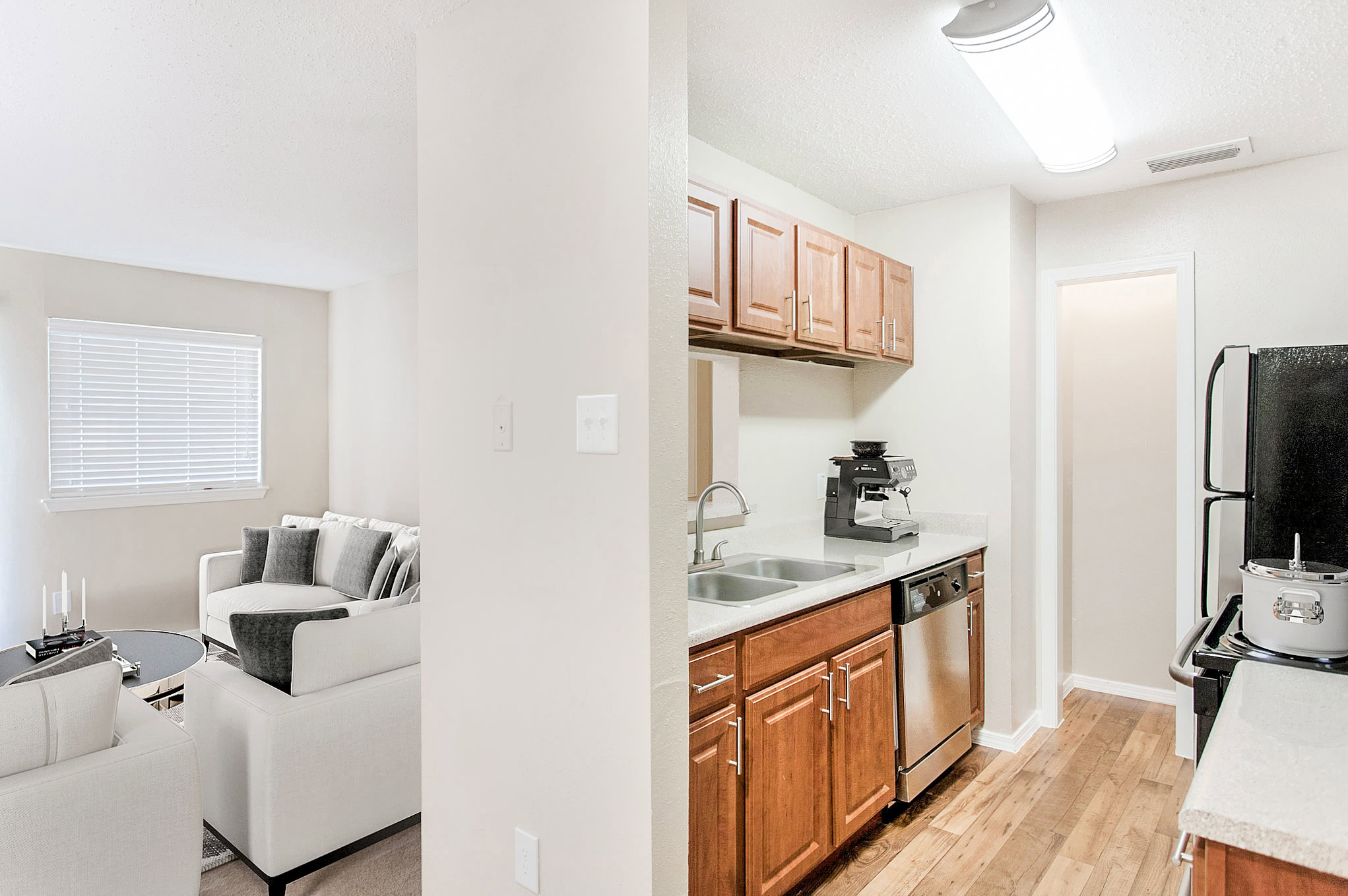 Kitchen and living area inside a Mckinney Texas apartment featuring wood cabinets, stainless steel appliances, and a bright, modern living room.