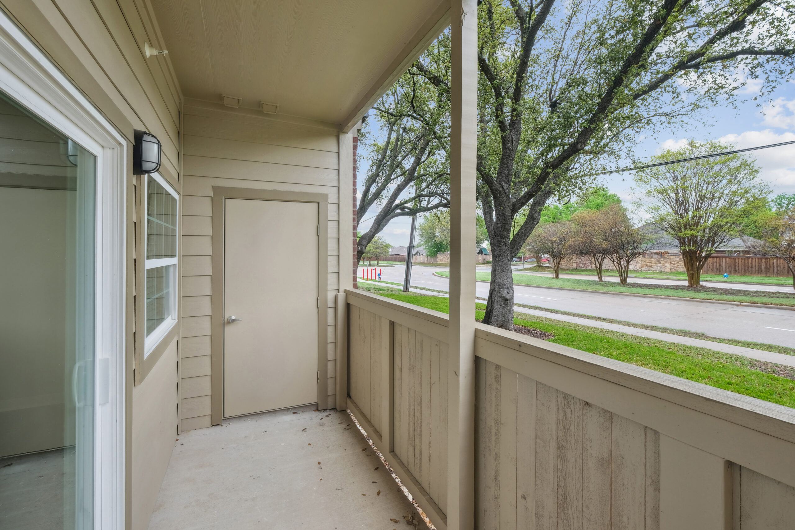 Private first floor balcony at an apartment in Mckinney Texas featuring fenced privacy panels, storage closet, and views of tree-lined streets.