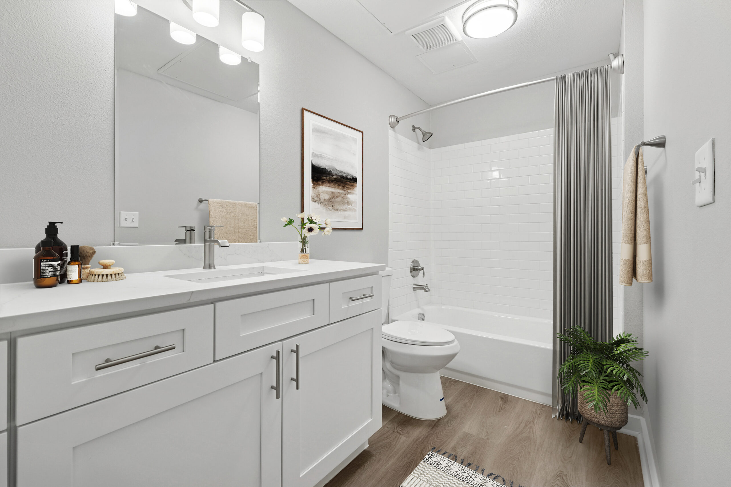 Modern bathroom in Mckinney Texas with white shaker cabinets, quartz countertop, subway tile tub surround, and wood-style floors.